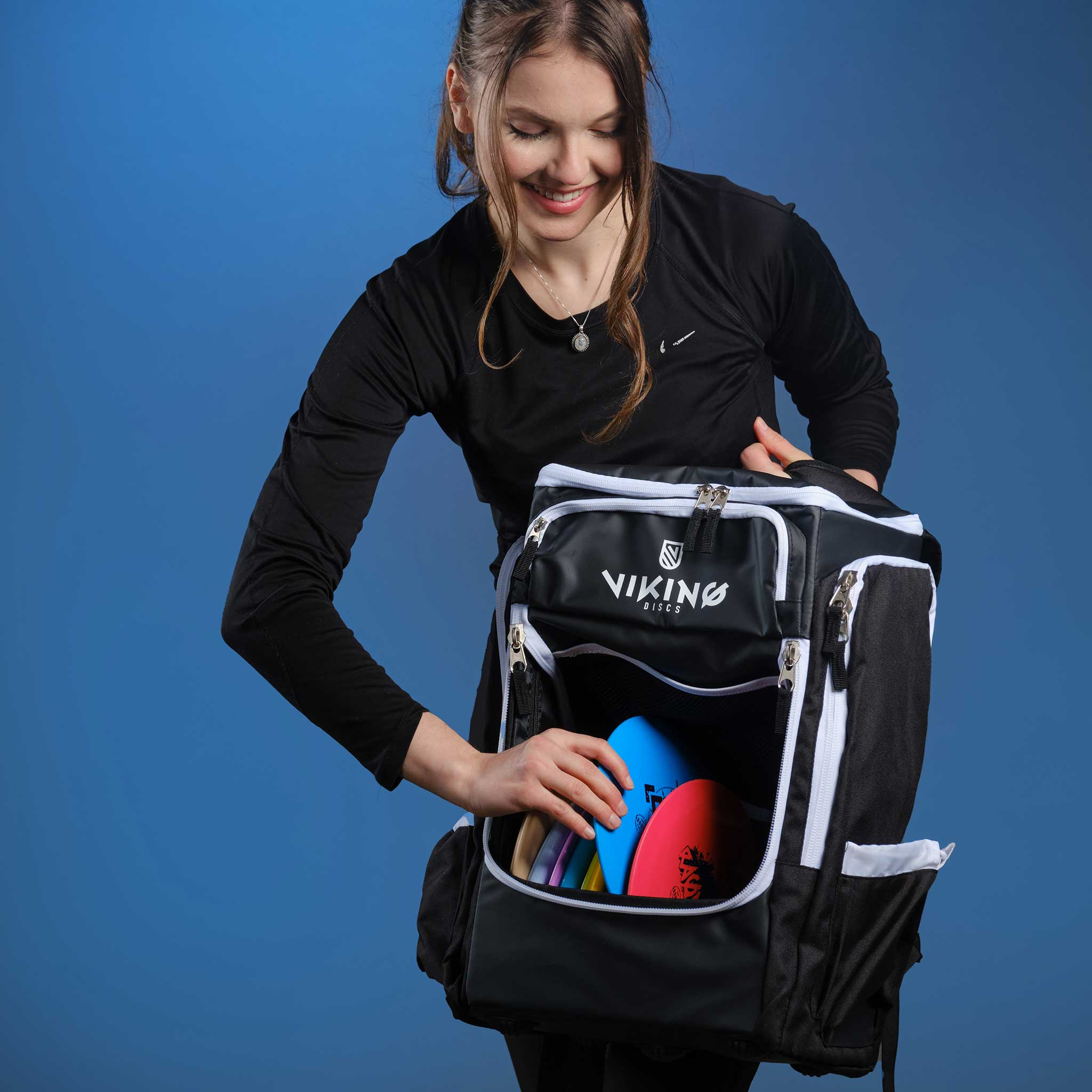 Kobieta pakuje kolorowe frisbee do czarnego plecaka.