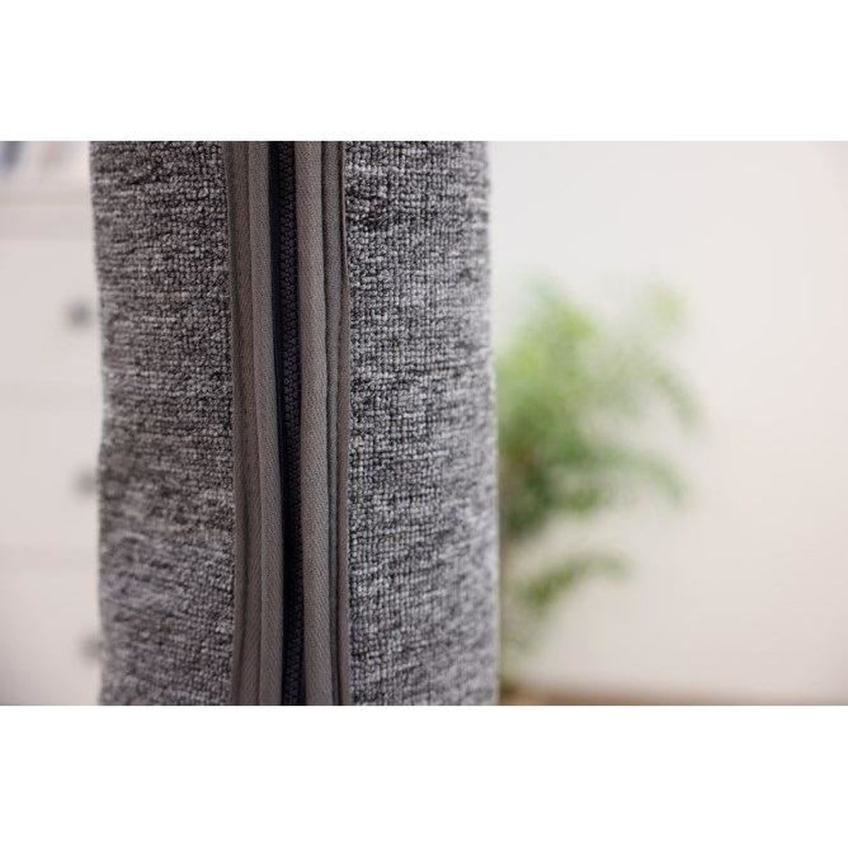Graues Textil mit Reißverschluss im Detail, unscharfer Hintergrund mit Pflanze.