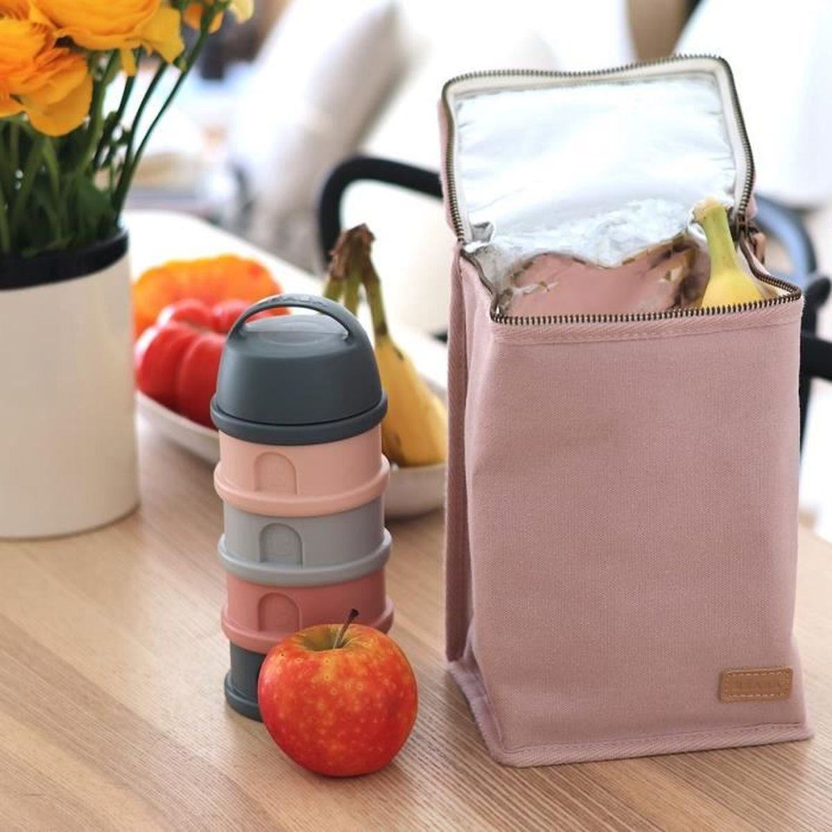 Ein gestapeltes Lunchbox-Set, ein Apfel und eine rosa Lunchtasche auf einem Holztisch.