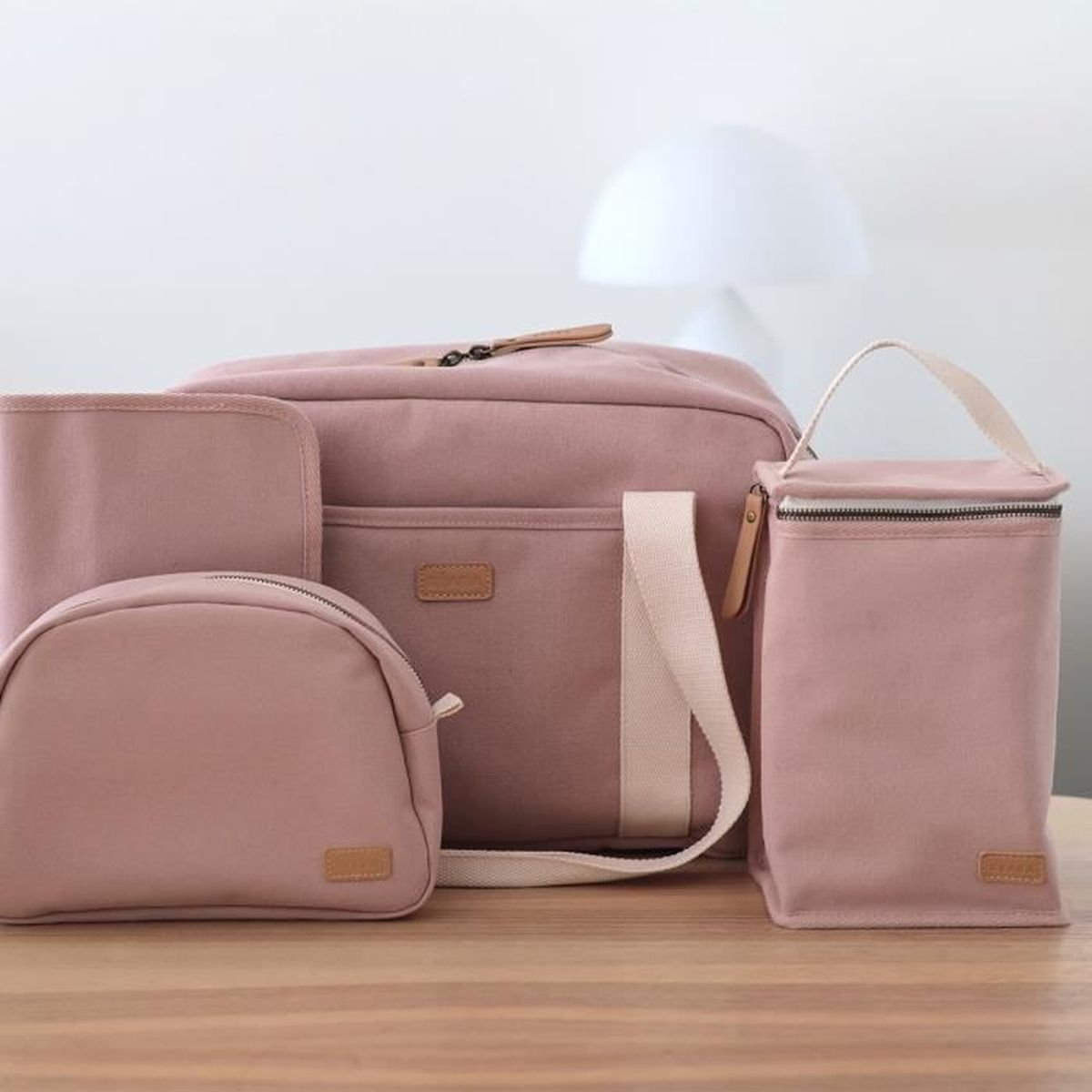 Fünf staubrosafarbene Taschen und Beutel in verschiedenen Größen auf einem Holztisch.