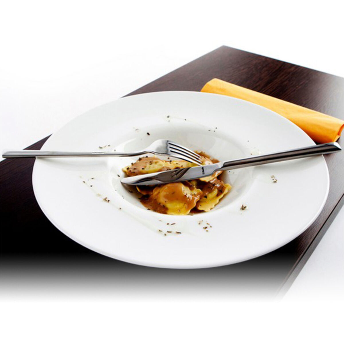 Ein weißer Teller mit Ravioli in Soße, darauf liegen Messer und Gabel.
