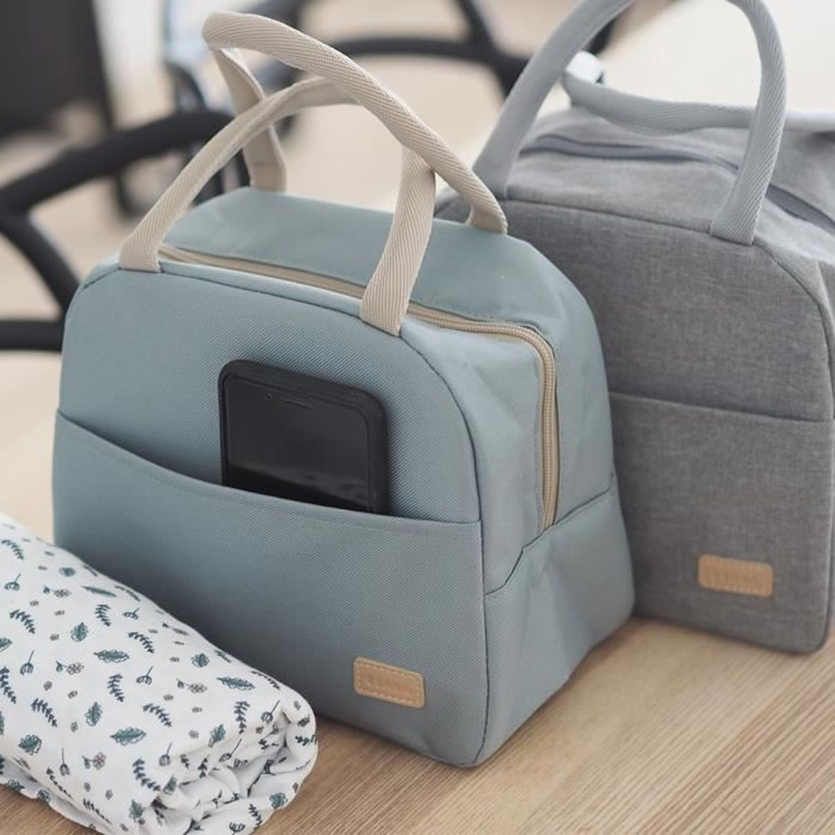 Zwei Lunchtaschen, eine hellblau mit Handy, eine grau. Daneben eine gerollte Decke.