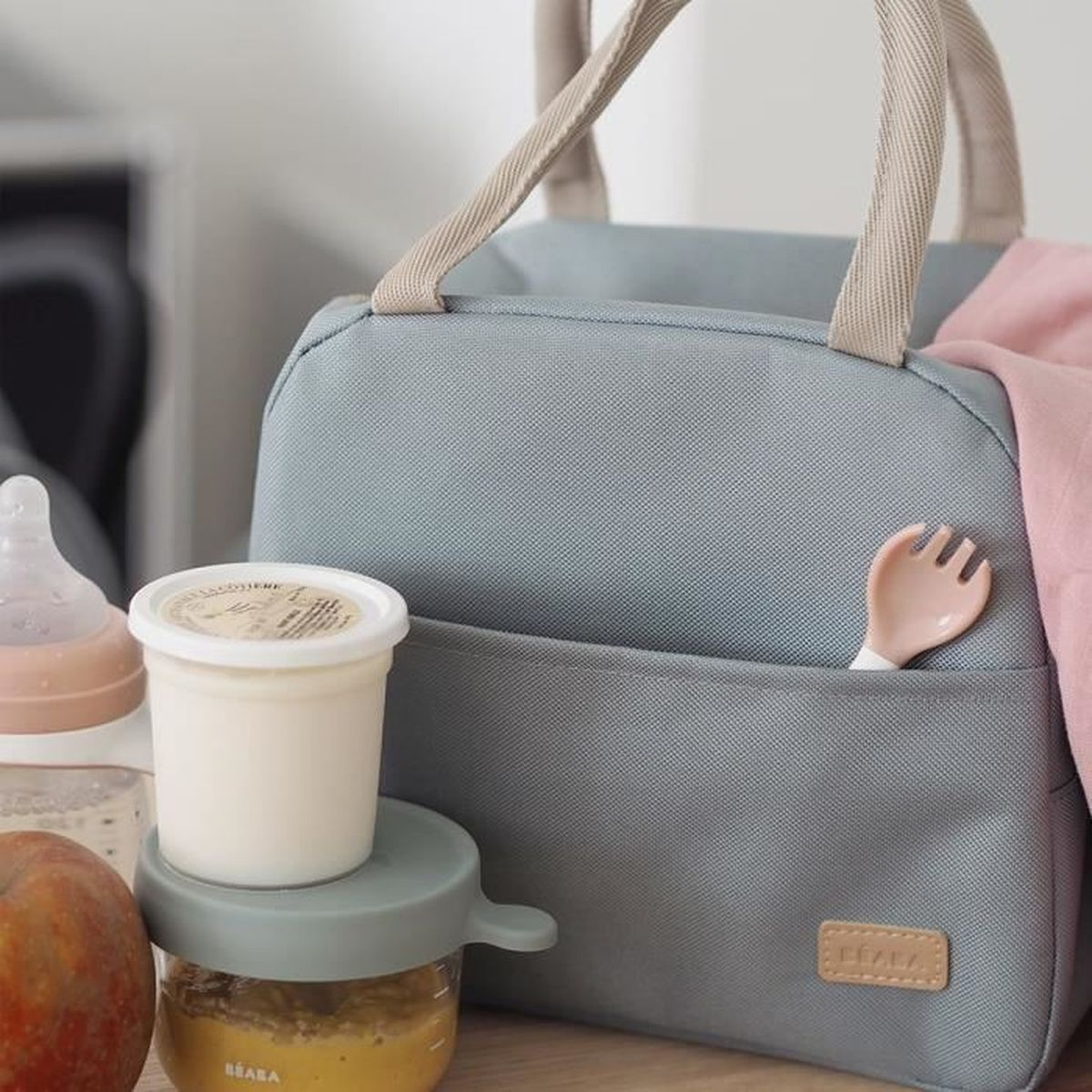 Eine graue Lunchtasche mit Babyflasche, Apfel und Essensbehältern.
