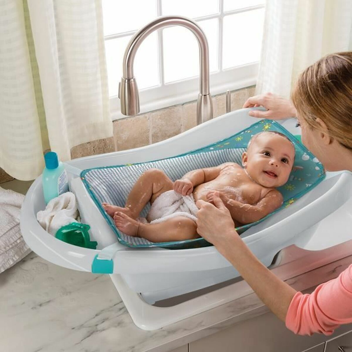 Ein Baby liegt in einer Babybadewanne, ein Erwachsener hilft beim Waschen.