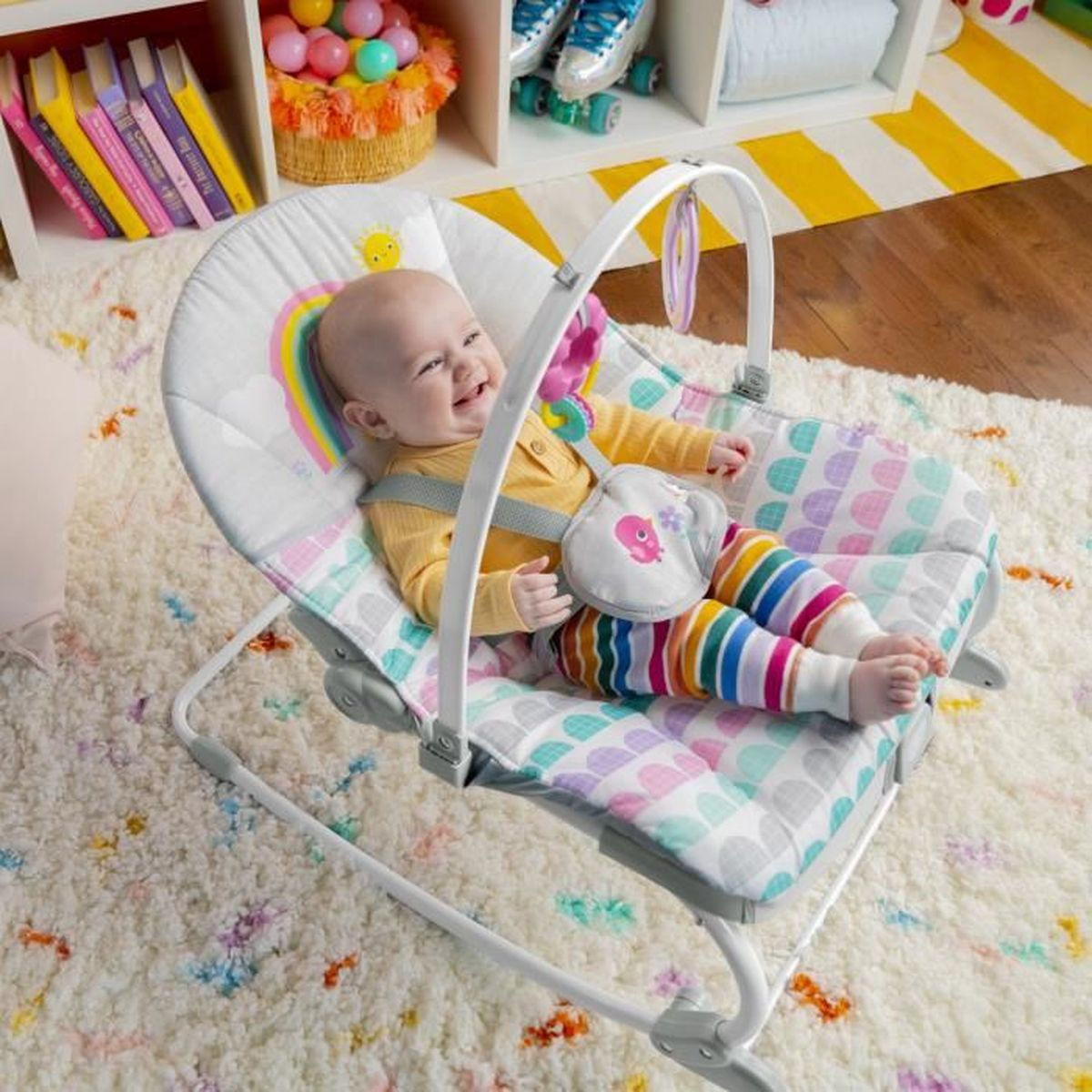 Ein Baby lacht in einer bunten Babyschaukel auf einem flauschigen Teppich.
