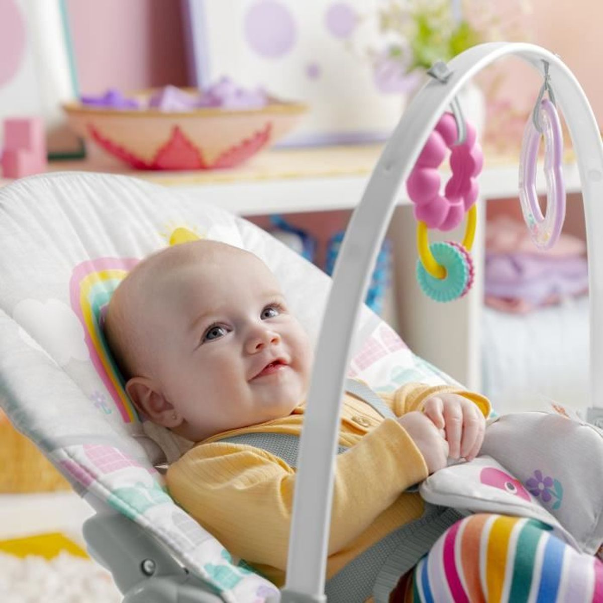 Ein Baby liegt in einer bunten Babyschaukel und schaut nach oben.