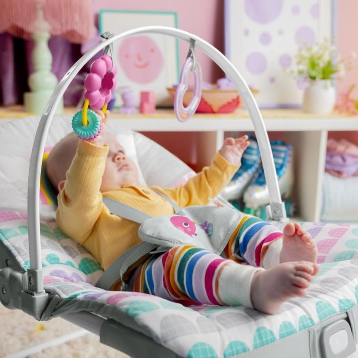 Ein Baby in einem bunten Babystuhl mit Spielzeug über sich.