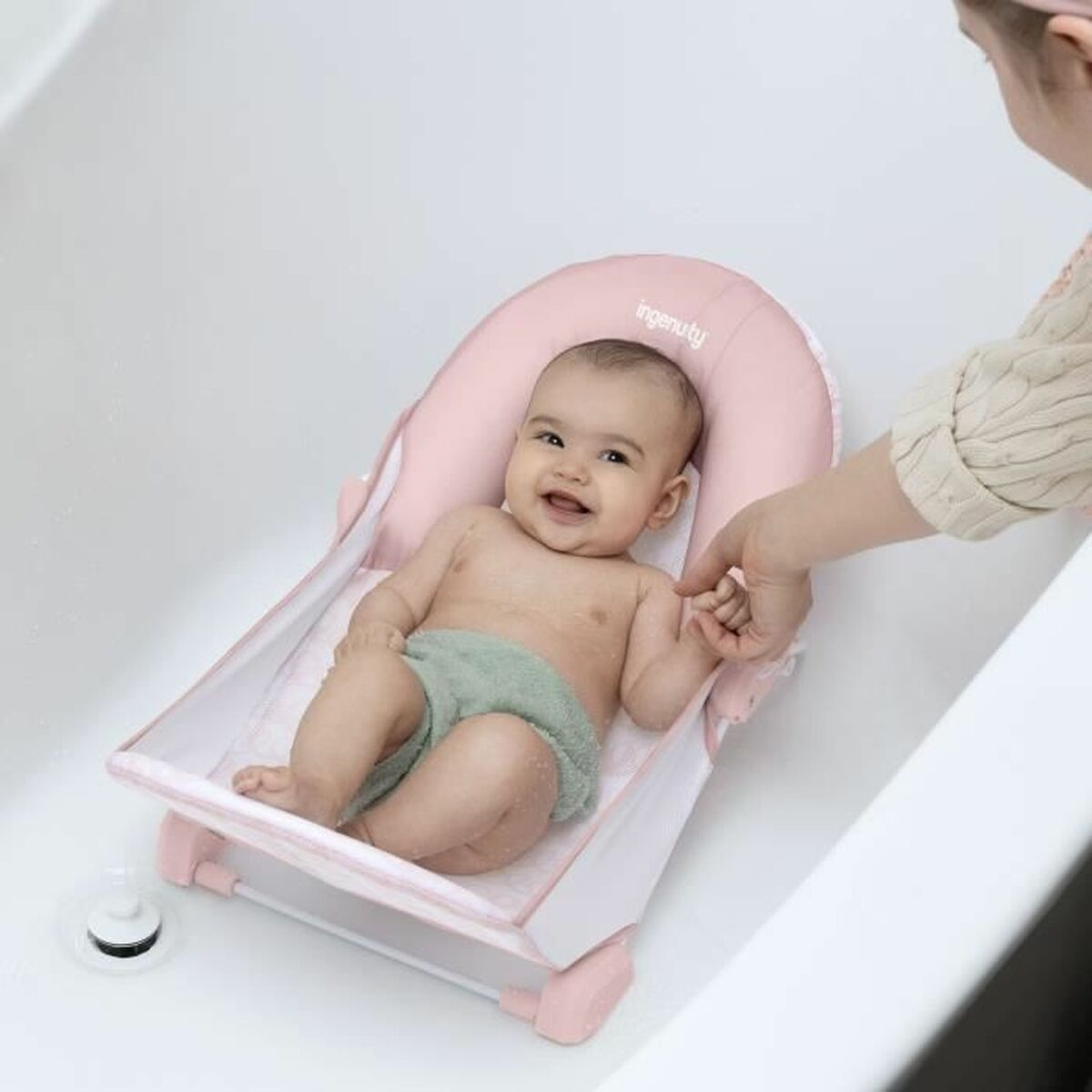 Ein Baby liegt in einer rosa Babybadewanne in einer weißen Wanne. Eine Hand hält das Baby.