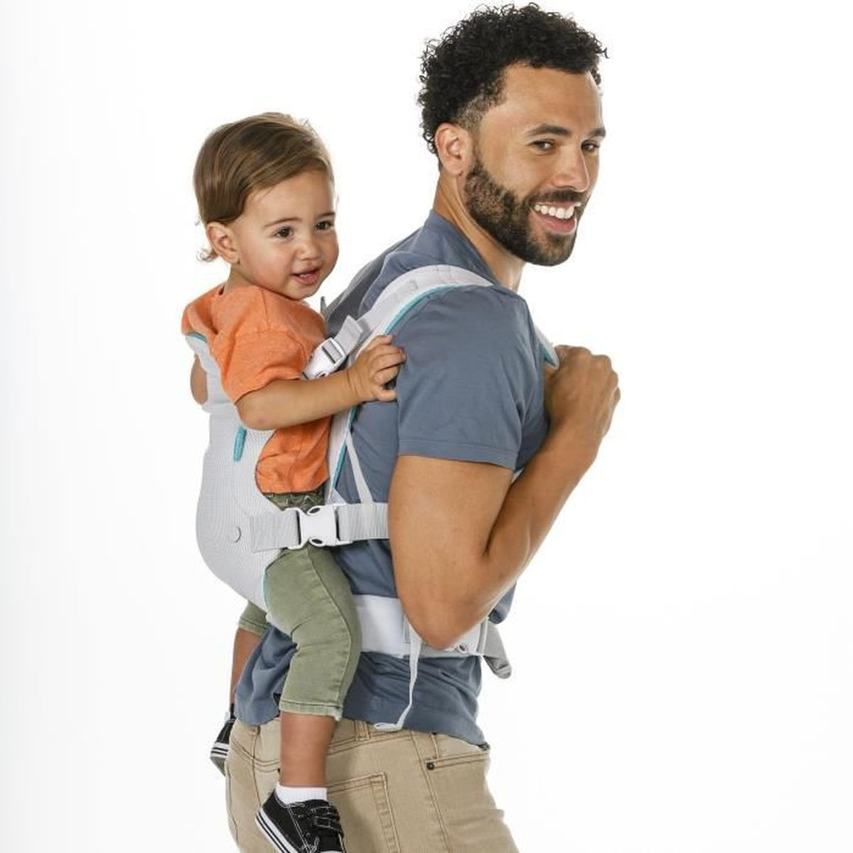 Mann trägt Baby im Rucksack. Baby orange Hemd, grüne Hose. Mann graues Hemd, beige Hose.