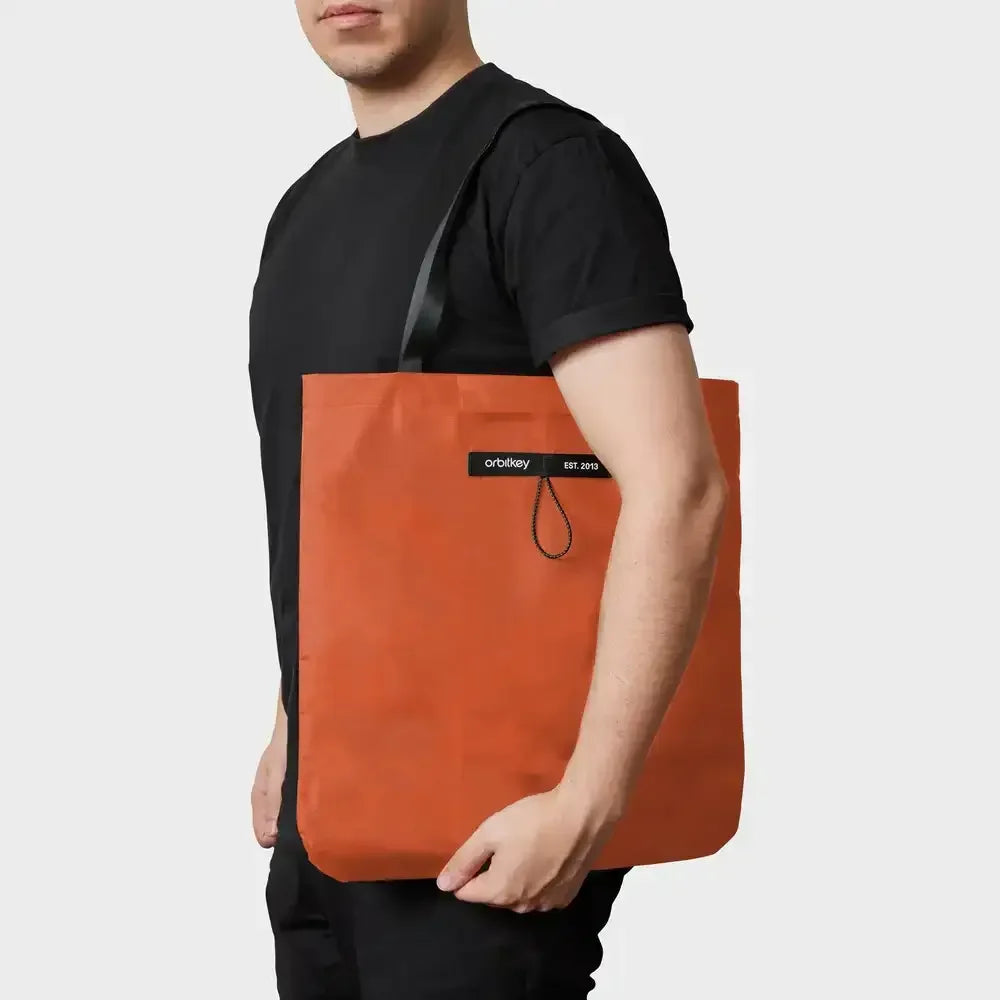 Mężczyzna trzymający pomarańczową torbę z logo "orbitkey EST. 2013".