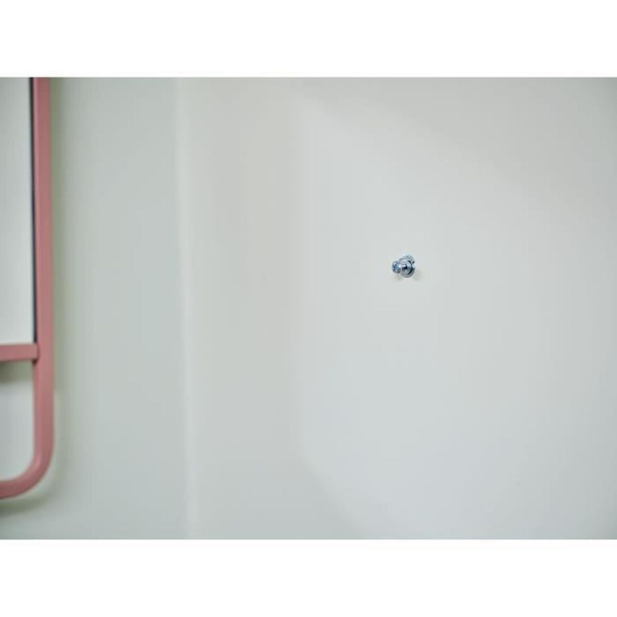 Ein silberner Bolzen mit Mutter an einer cremefarbenen Wand, mit einem rosafarbenen Rahmen links.
