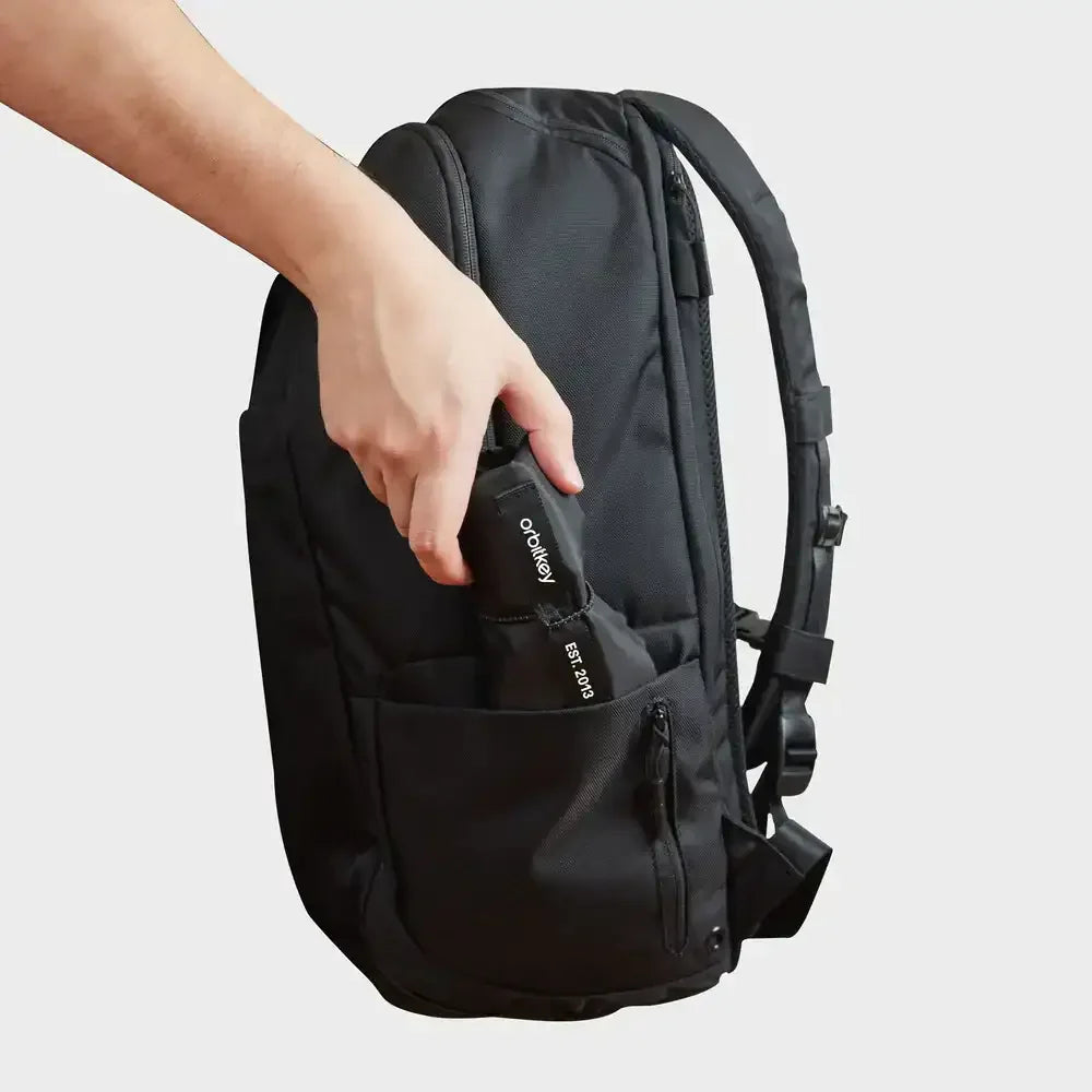 Ręka wkłada czarny przedmiot z napisem "orbitkey" do czarnej torby.