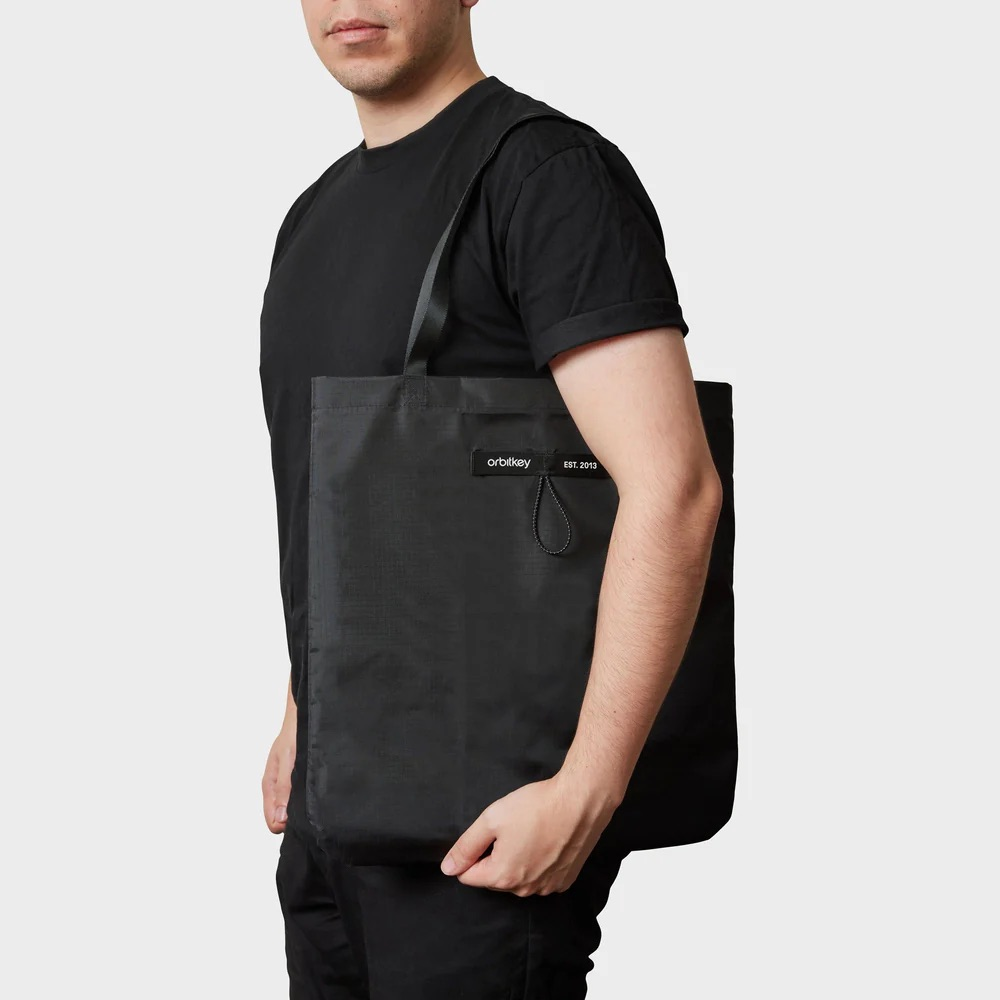 Mężczyzna w czerni nosi czarną torbę z logo Orbitkey.