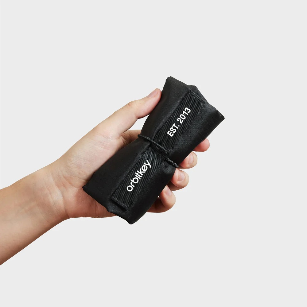 Dłoń trzyma czarne etui Orbitkey z napisem "EST. 2013".