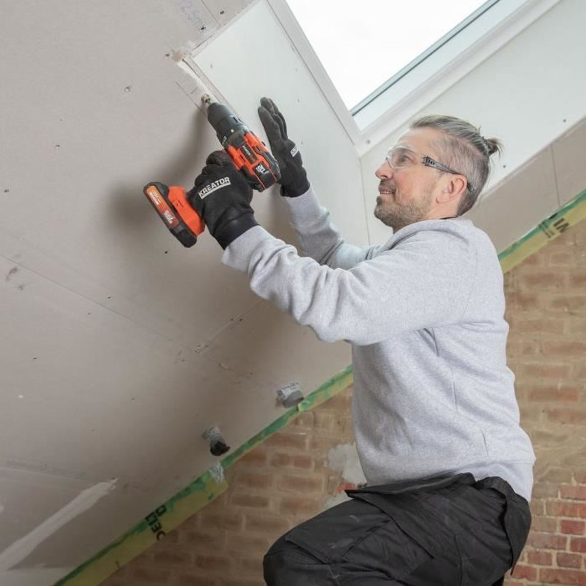 Mann mit Bohrmaschine montiert Gipskarton an Dachschräge.