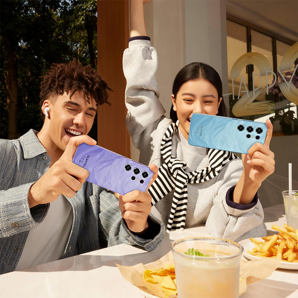 Pareja sonriente mostrando teléfonos morados y azules al aire libre. Comida en mesa.