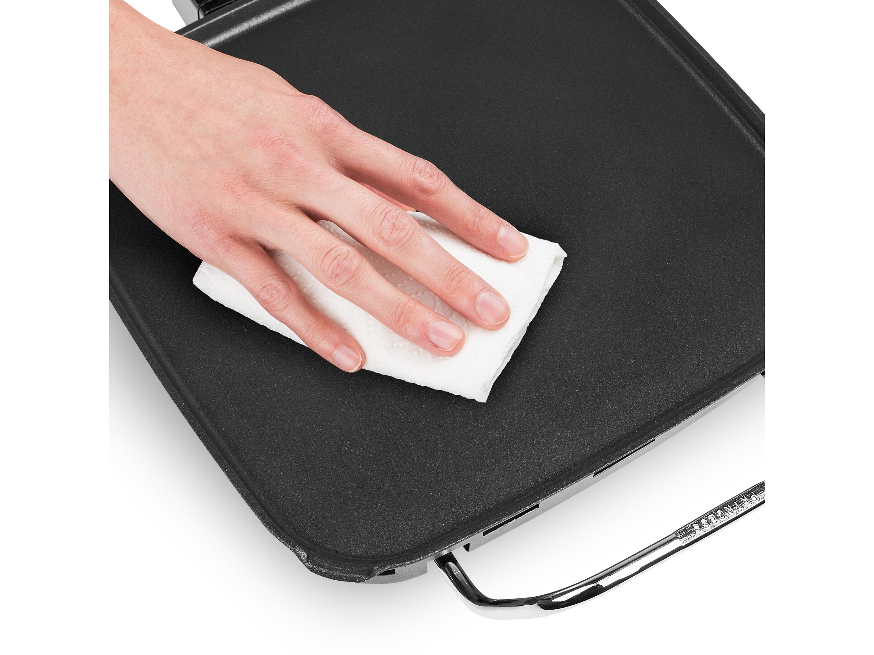 Una mano limpia una plancha negra con un paño blanco.