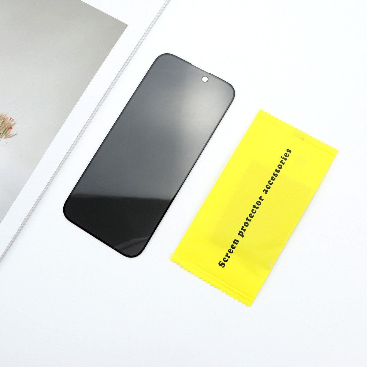 Eine schwarze Smartphone-Displayschutzfolie liegt neben einer gelben Packung mit der Aufschrift 'Screen protector accessories'.