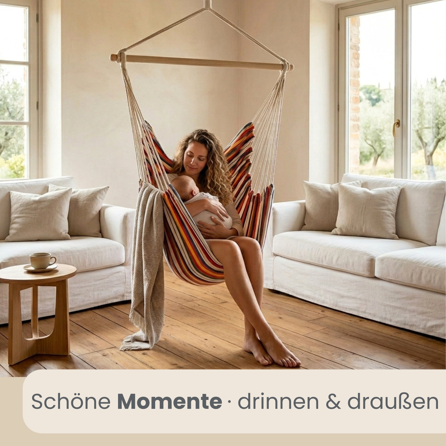 Eine Frau hält ein Baby in einem bunten Hängesessel in einem hellen Raum mit Sofas.