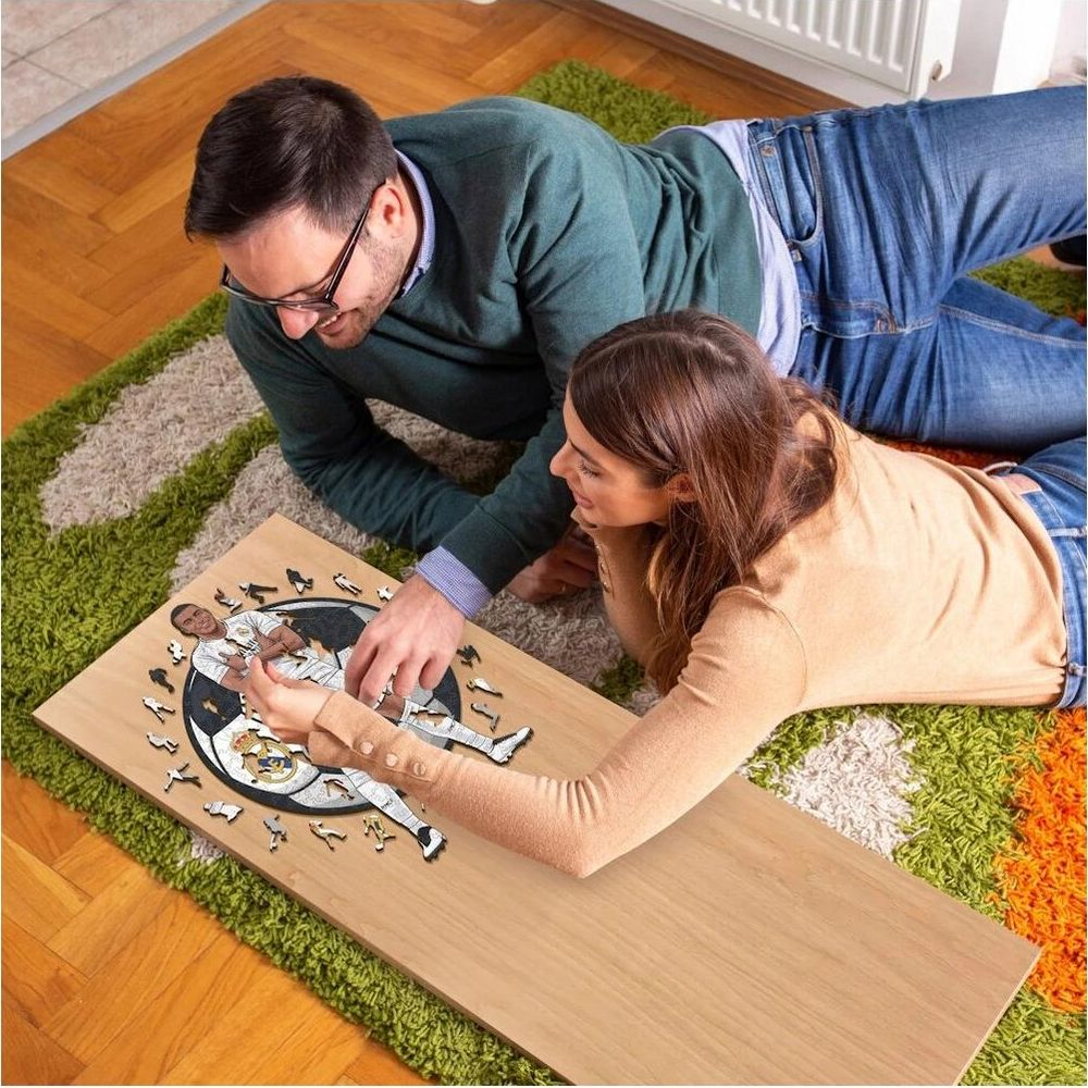 Ein Paar liegt auf einem Teppich und puzzelt ein Bild eines Fußballspielers.
