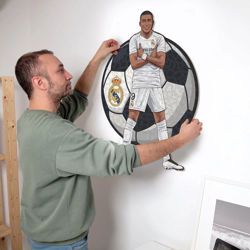 Ein Mann hängt ein Fußball-Puzzle mit einem Spieler in Weiß an die Wand.