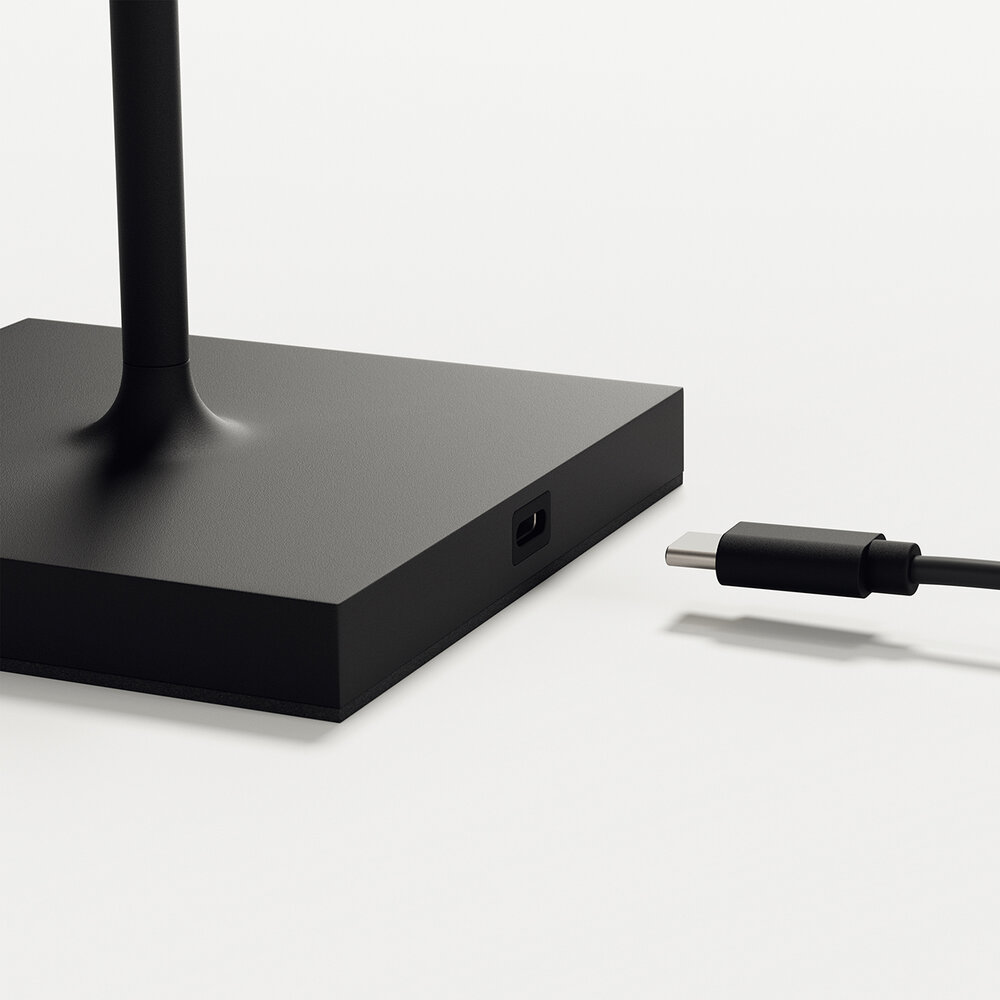 Ein schwarzes USB-C-Kabel nähert sich einer Buchse an der Basis einer schwarzen Lampe.