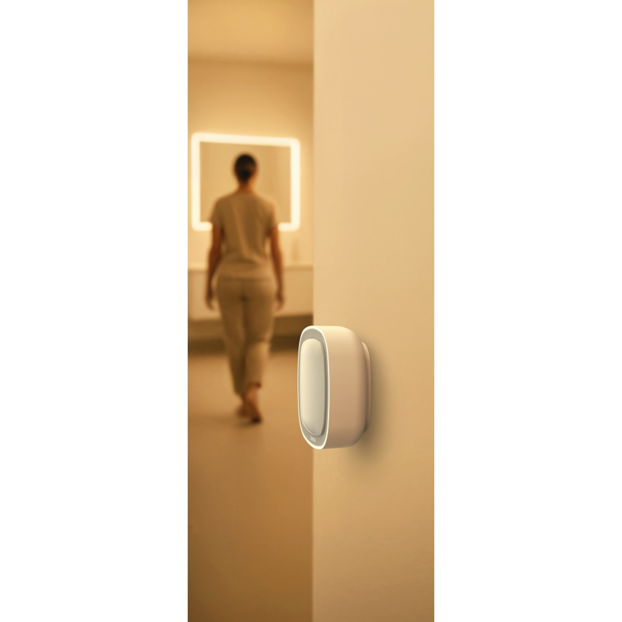 Una lampada da comodino in primo piano, una persona cammina verso uno specchio illuminato.