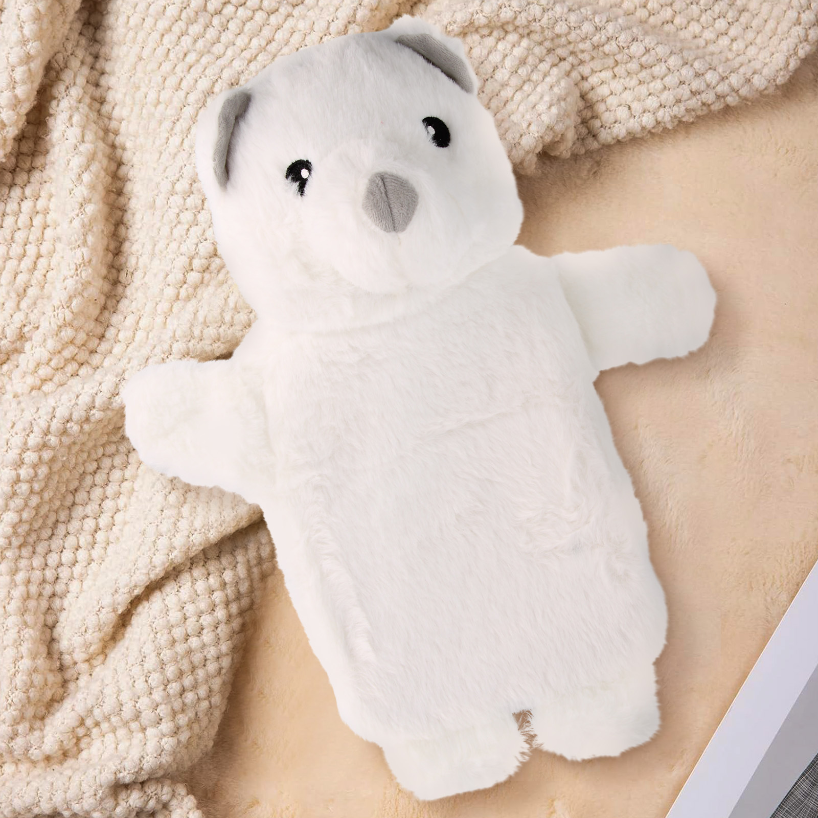 Copri borsa dell'acqua calda a forma di orso bianco con orecchie e naso grigi su coperta color crema.