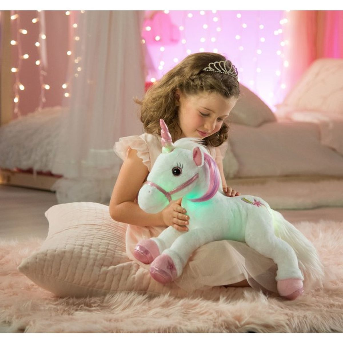 Una niña con tiara sostiene un peluche de unicornio brillante sobre una alfombra rosa.