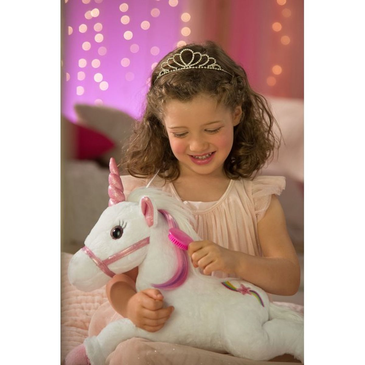 Una niña con tiara cepilla un unicornio de peluche blanco con melena rosa.