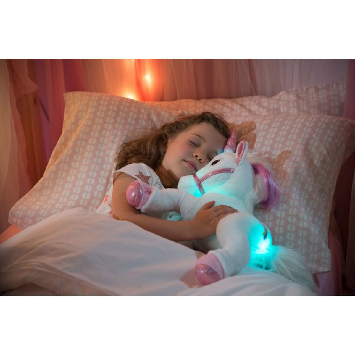 Una niña duerme en la cama, abrazando a un unicornio de peluche blanco con crin rosa y luces azules brillantes.