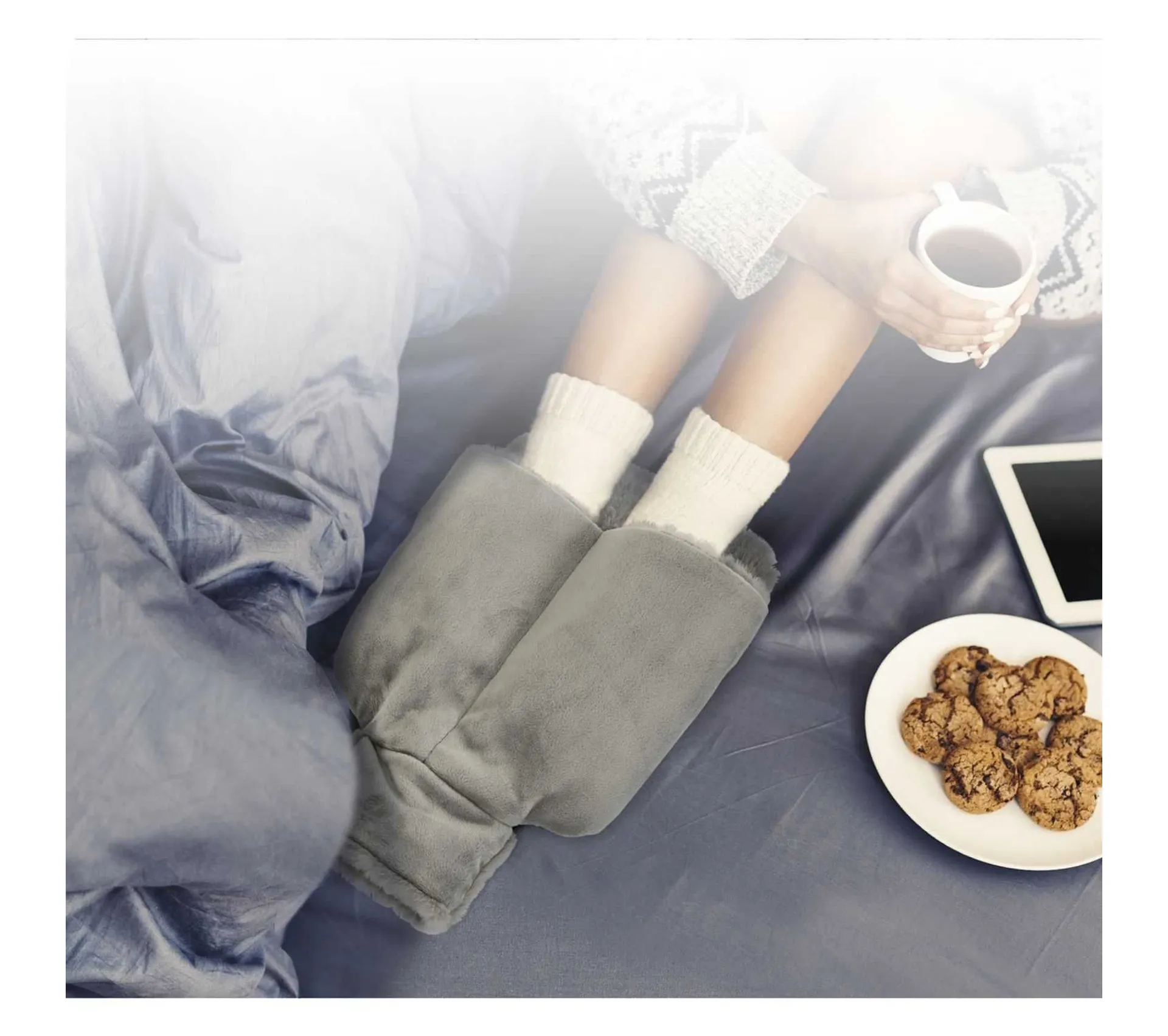 Pantofole grigie, calzini bianchi, tazza di tè e biscotti su un letto.
