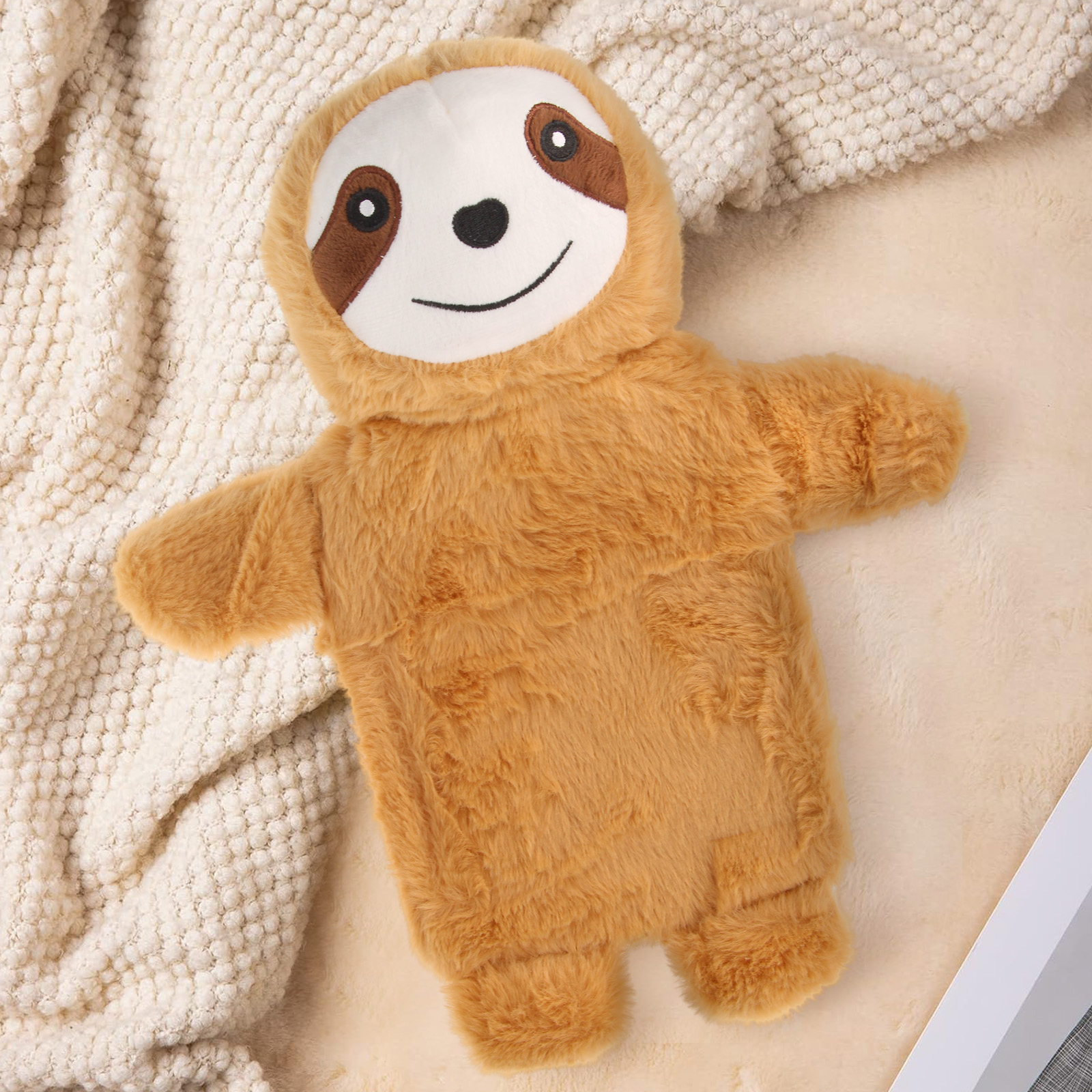 Una coperta marrone di peluche a forma di bradipo per borsa dell'acqua calda giace su una coperta color crema.