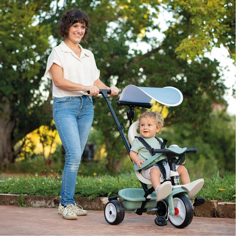 Una donna spinge un bambino su un triciclo all'aperto.