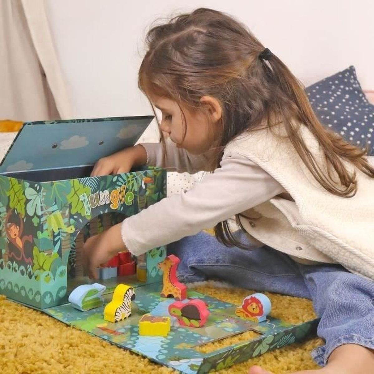 Ein kleines Mädchen spielt mit einem Dschungel-Spielzeugset auf einem Teppich.