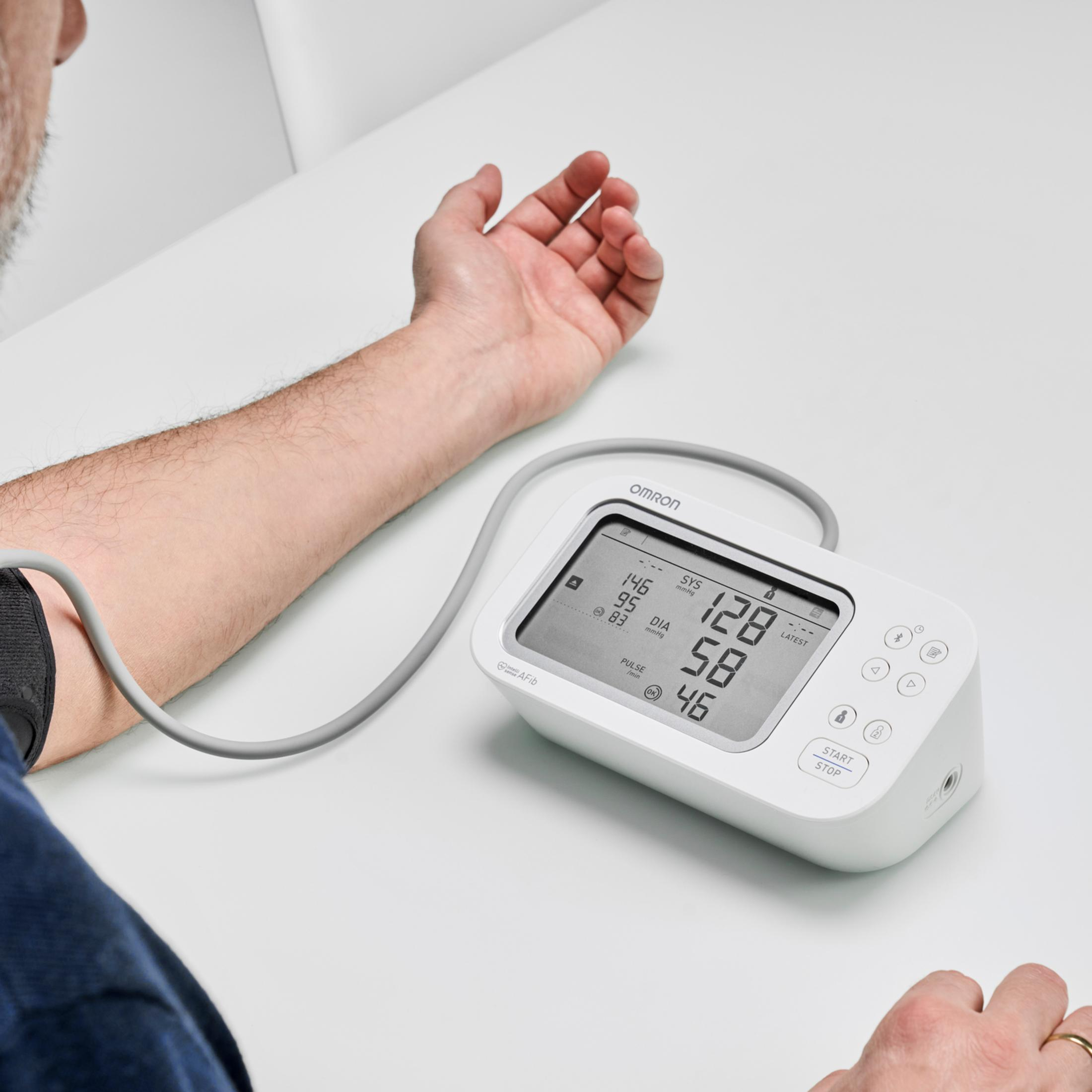 Een man meet zijn bloeddruk met een Omron apparaat. Het display toont 146/95 mmHg en 46 bpm.
