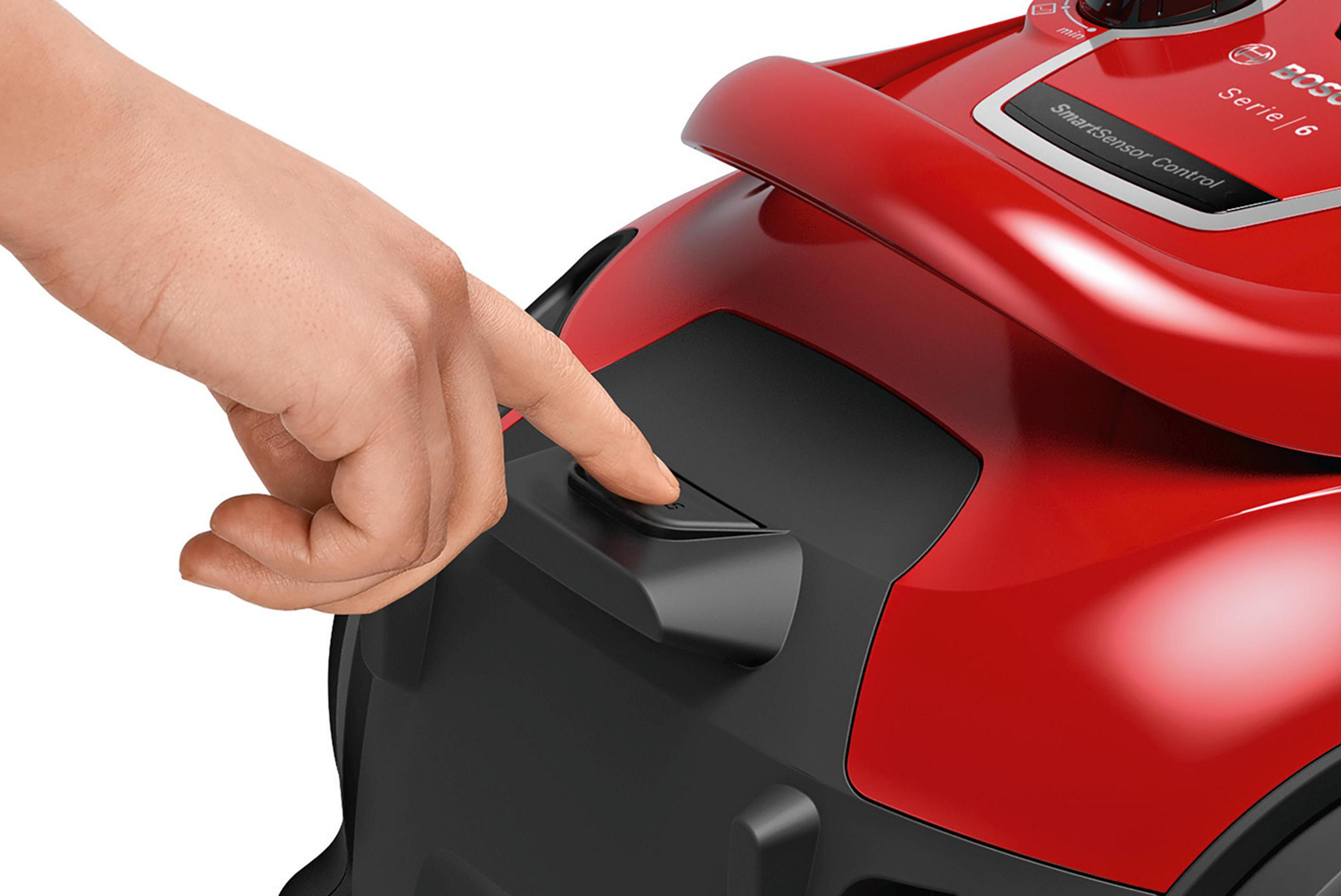 A hand presses a button on a red Bosch vacuum cleaner.