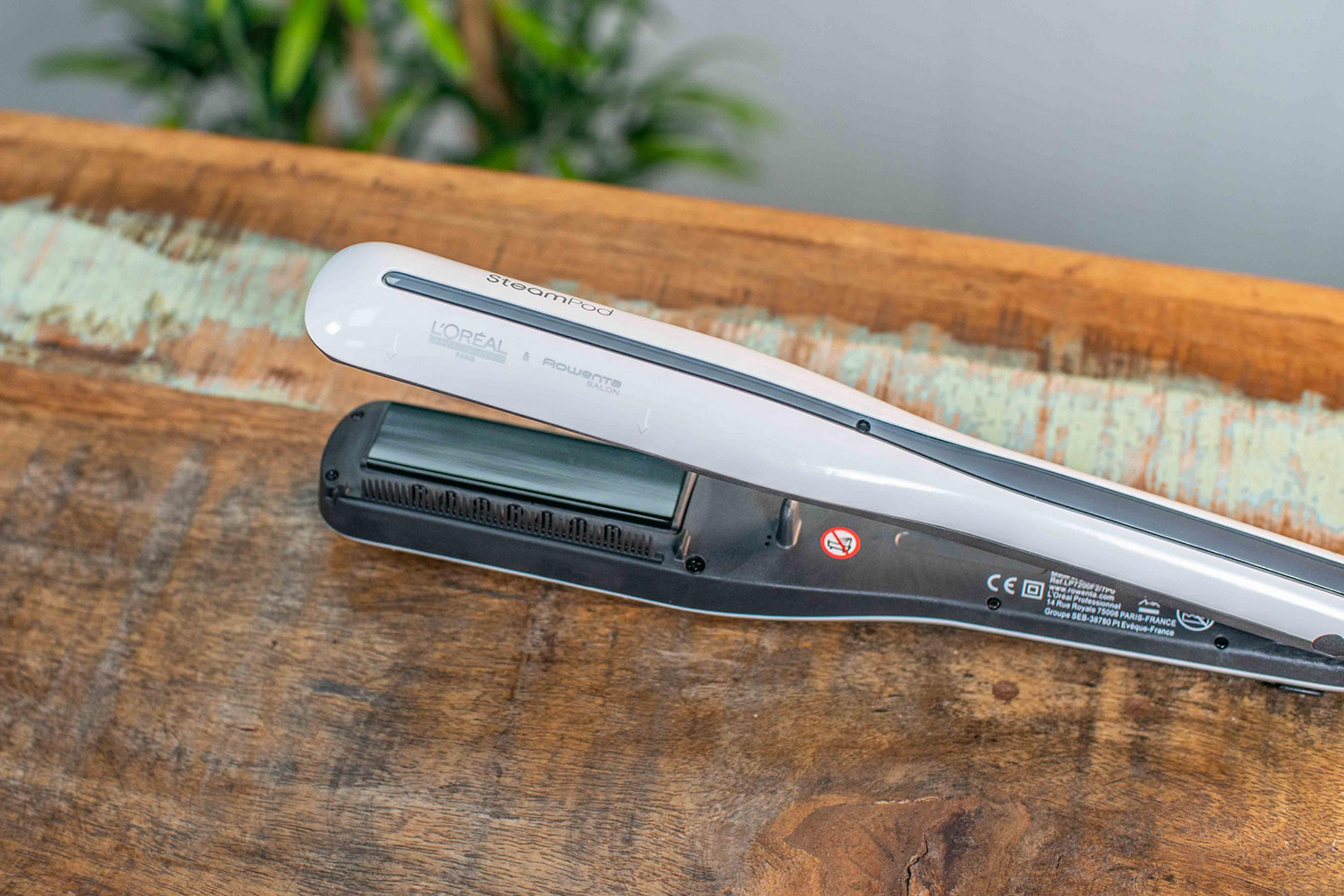 Una plancha de pelo L'Oréal SteamPod blanca con logo Rowenta sobre mesa de madera.