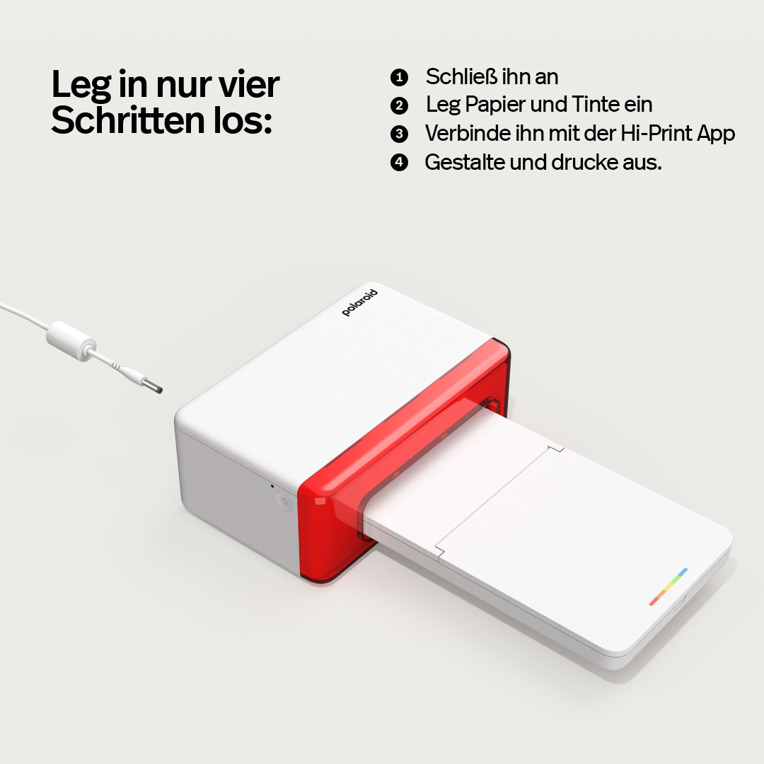 Drukarka Polaroid z czerwonym slotem i białym podajnikiem, kabel w pobliżu.
