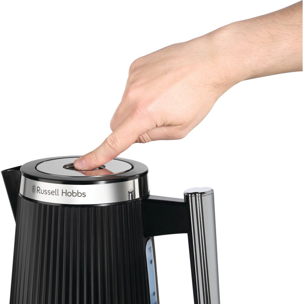 Eine Hand drückt auf den Knopf eines schwarzen Wasserkochers von Russell Hobbs.