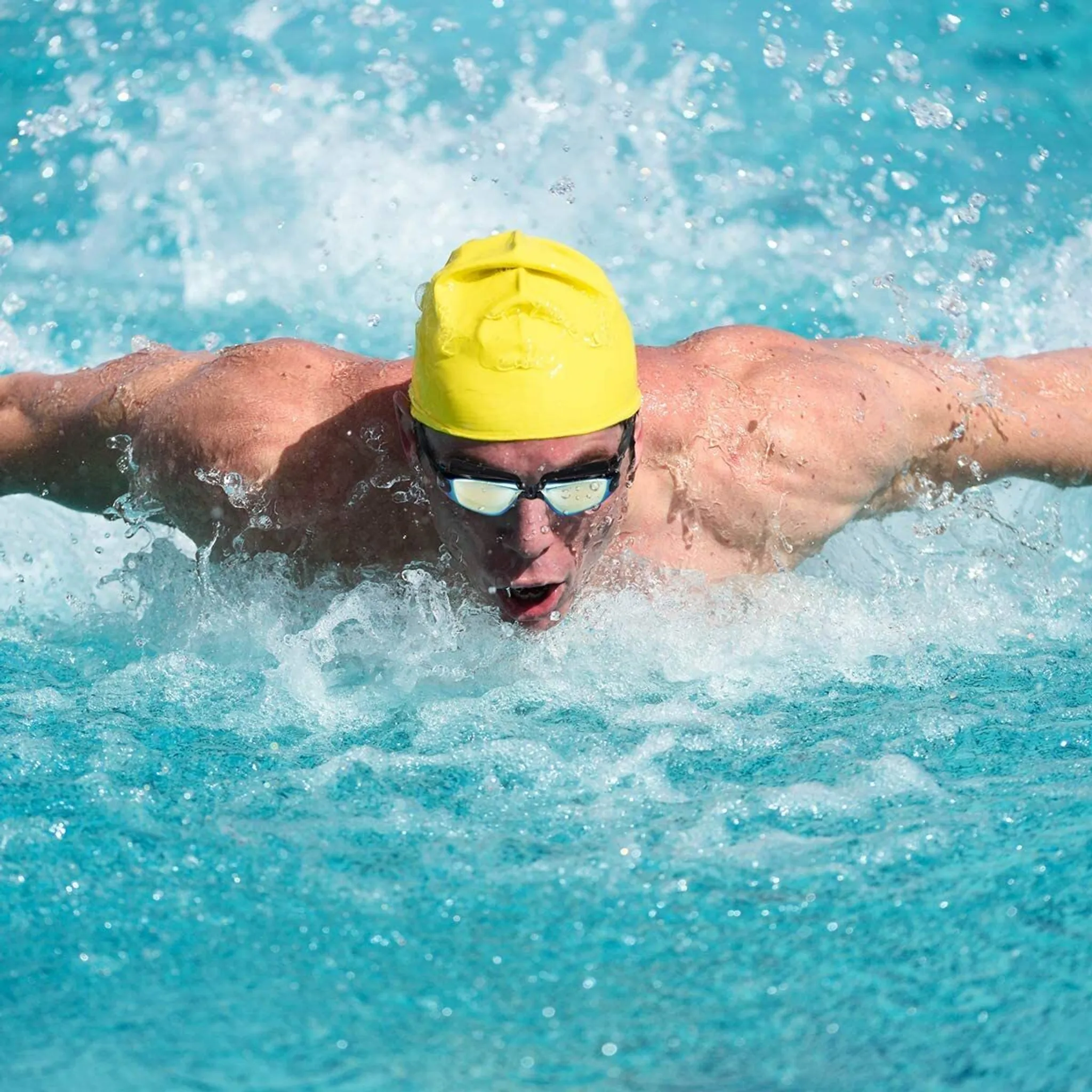 Ein Schwimmer in gelber Kappe und Schwimmbrille schwimmt Schmetterling.
