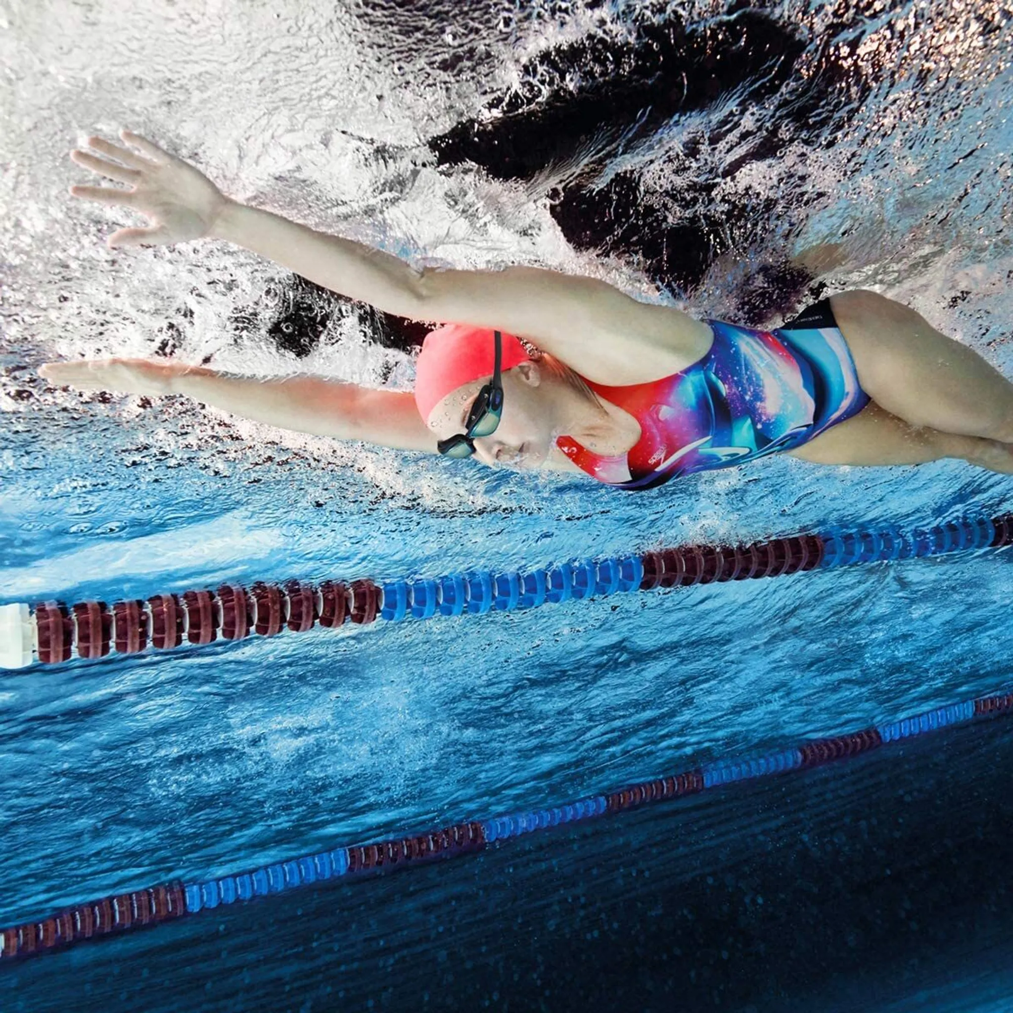 Eine Schwimmerin mit roter Badekappe schwimmt unter Wasser in einem Becken.