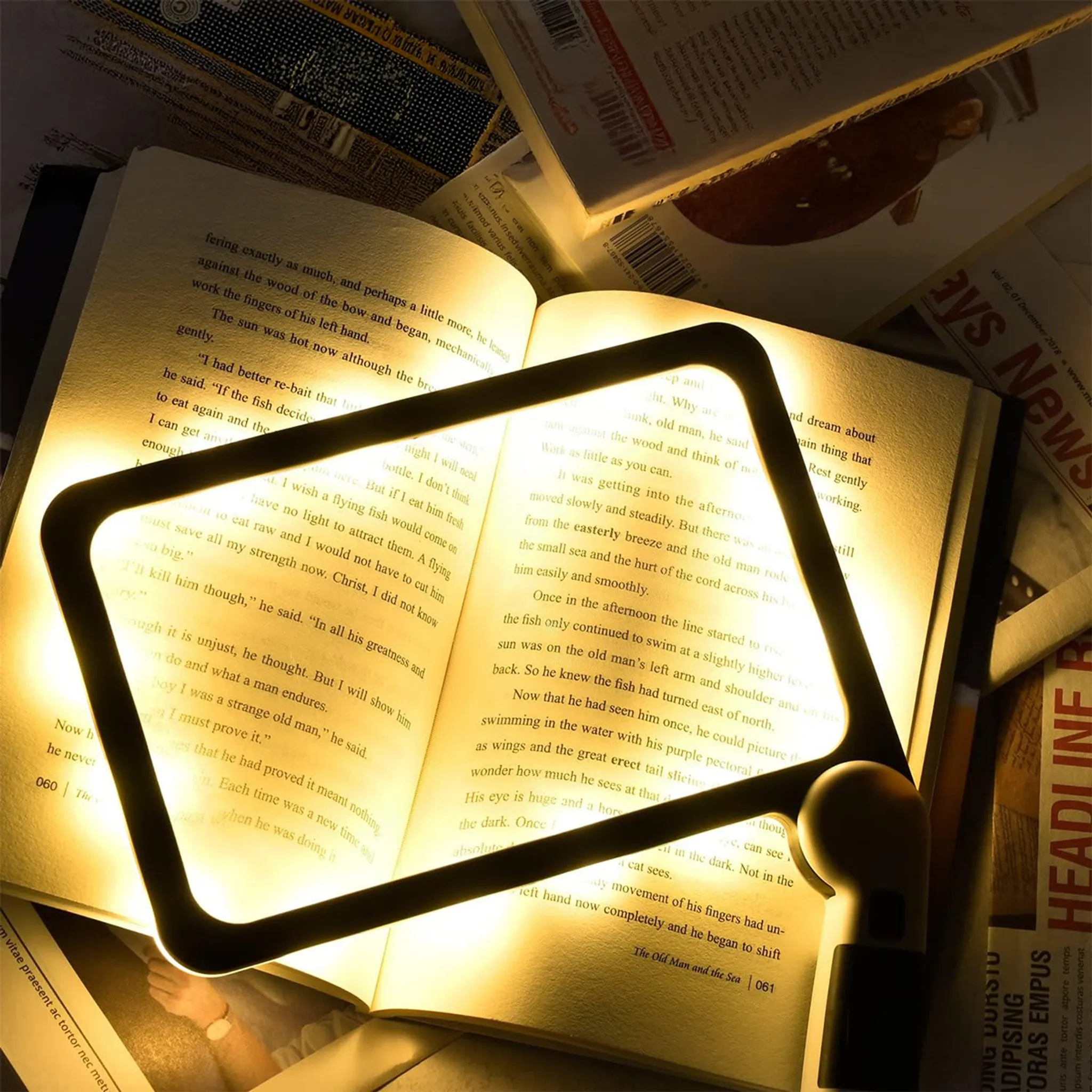 Ein aufgeschlagenes Buch wird von einer Dreiecklampe beleuchtet, umgeben von Zeitungen.