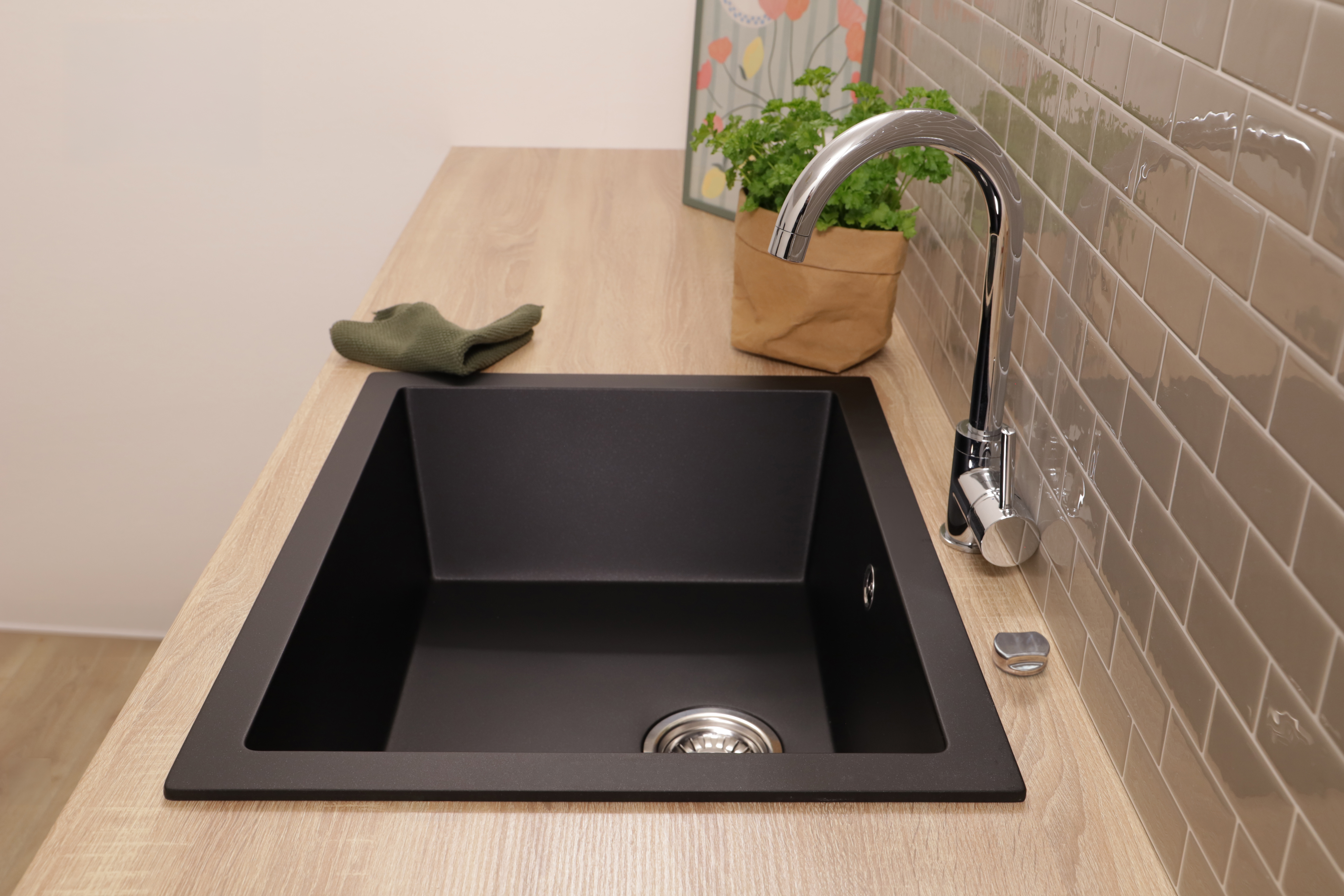 Ein schwarzes Spülbecken mit Chromarmatur auf einer Holzoberfläche, daneben eine Topfpflanze.