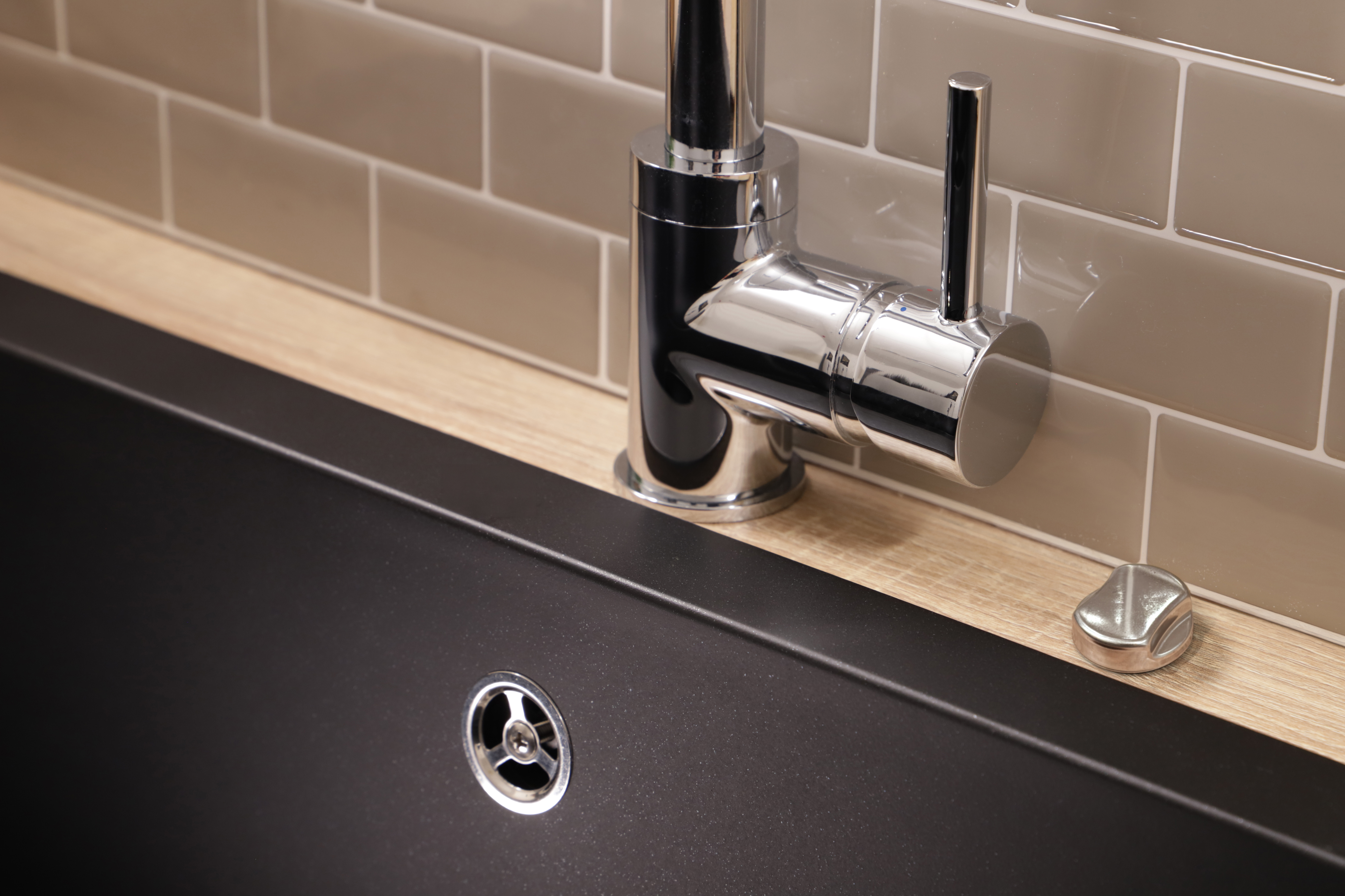 Ein moderner Küchenwasserhahn mit schwarzem Spülbecken und beiger Kachelrückwand.