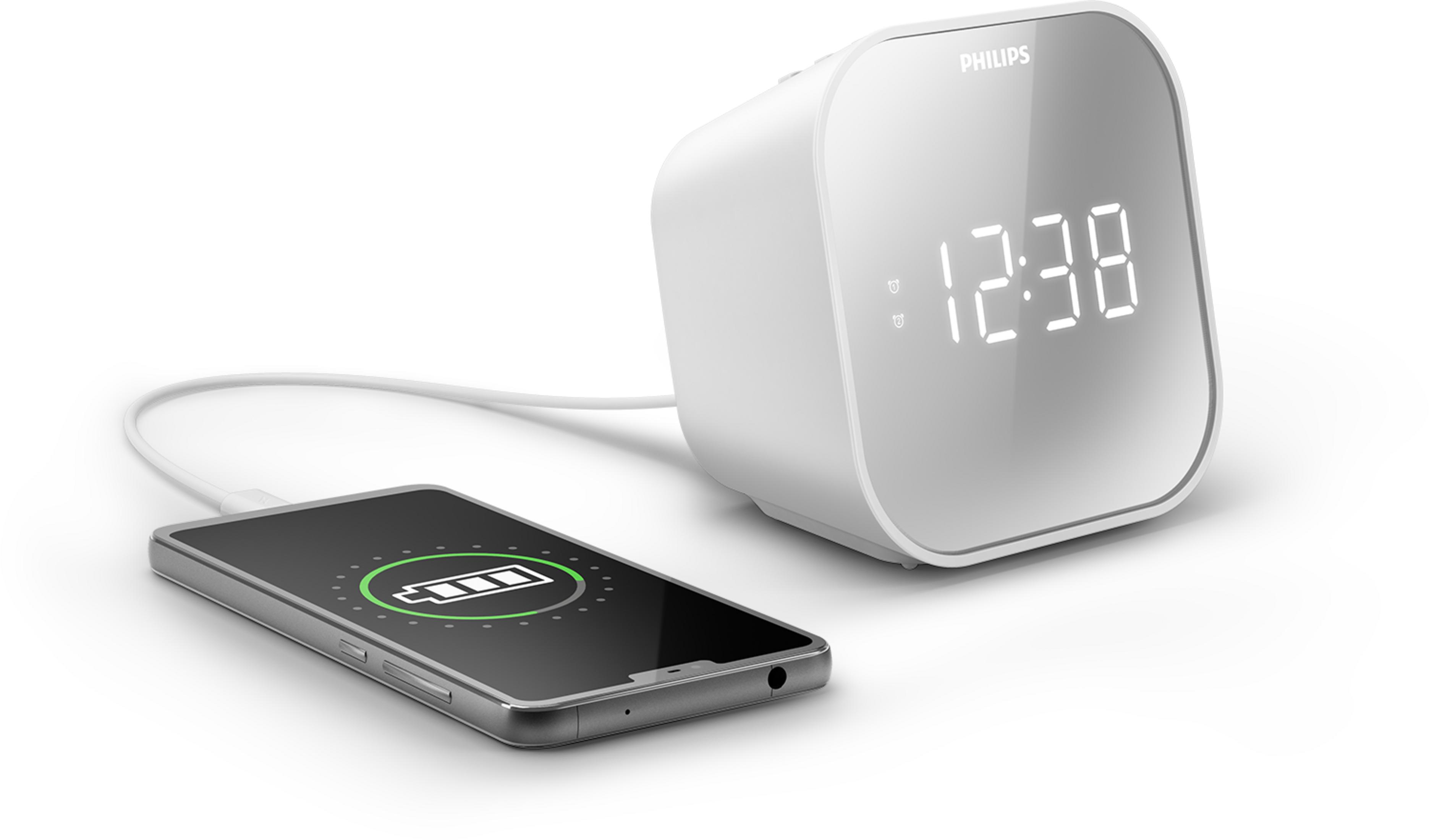 Un despertador Philips blanco con pantalla digital carga un smartphone.