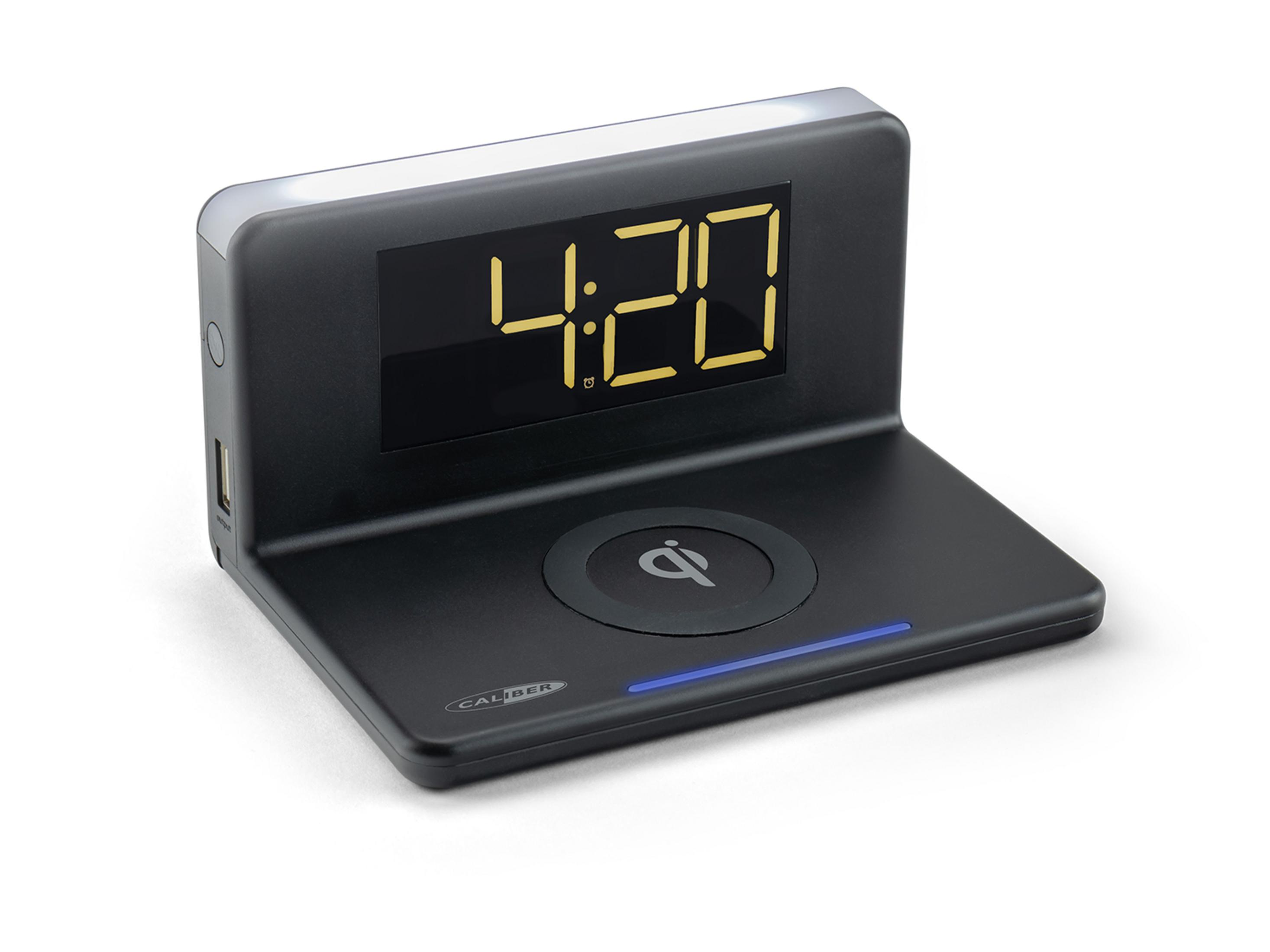 Black digital alarm clock with yellow display showing 4:20, Qi charging pad.