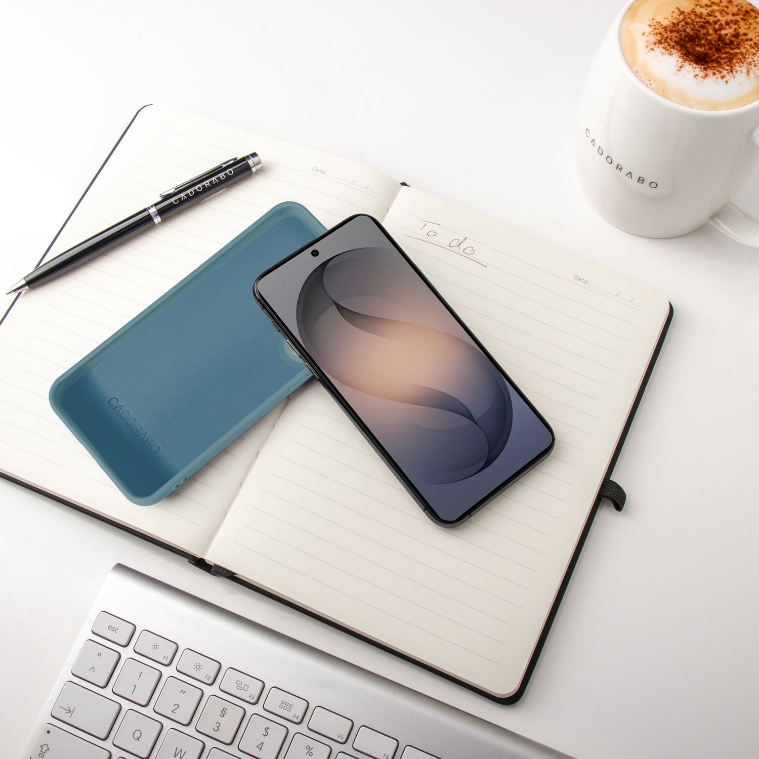 Ein Notizbuch mit einem Smartphone, einer Hülle, einem Stift und einer Kaffeetasse.