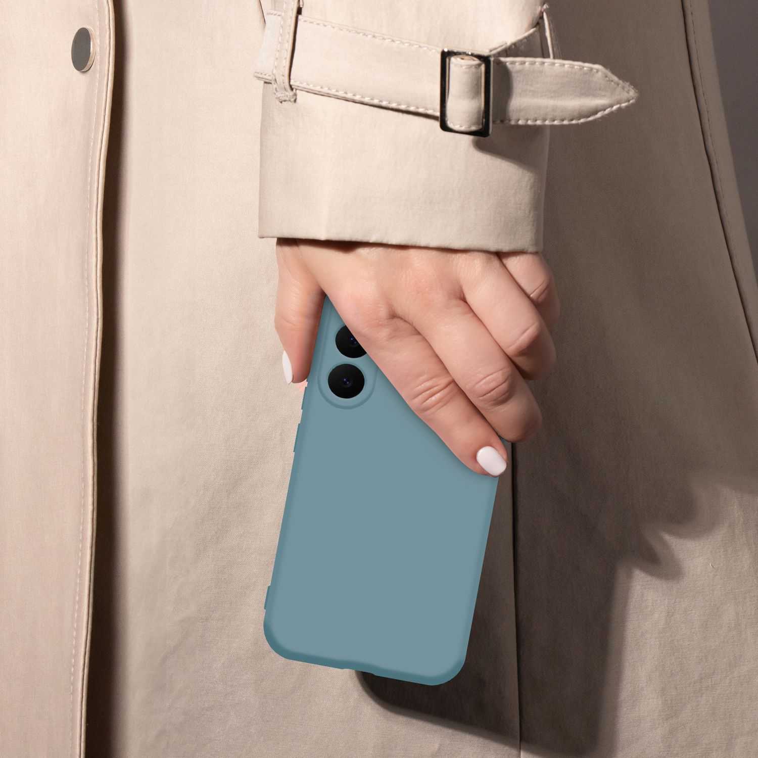 Eine Hand hält ein blaues Smartphone vor einem beigefarbenen Trenchcoat.