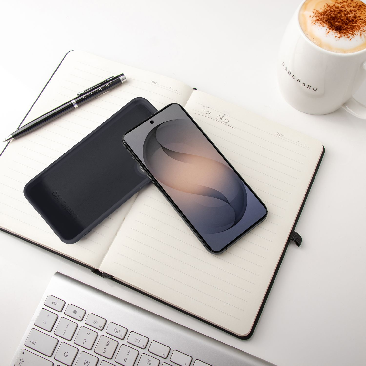 Ein Notizbuch mit Stift, Handy, Tastatur und Kaffee auf weißem Hintergrund.